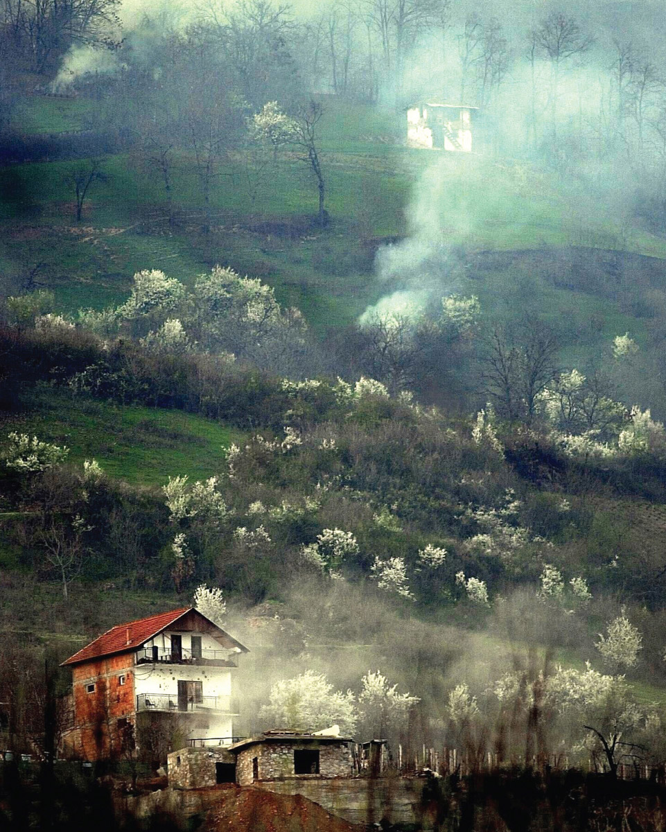 A photograph of houses on a hill dotted with smoke clouds.