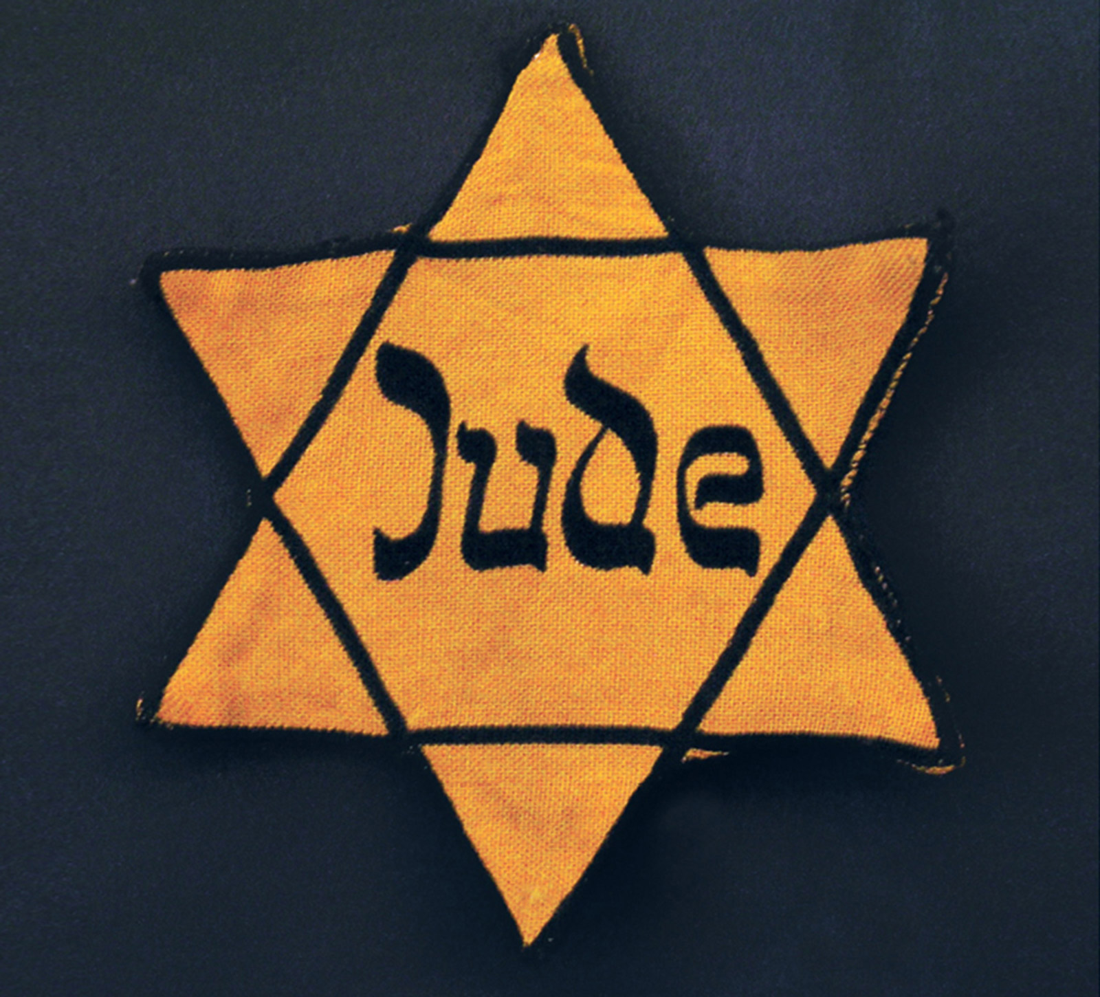 A photograph of a gold Star of David badge which reads “Jude,