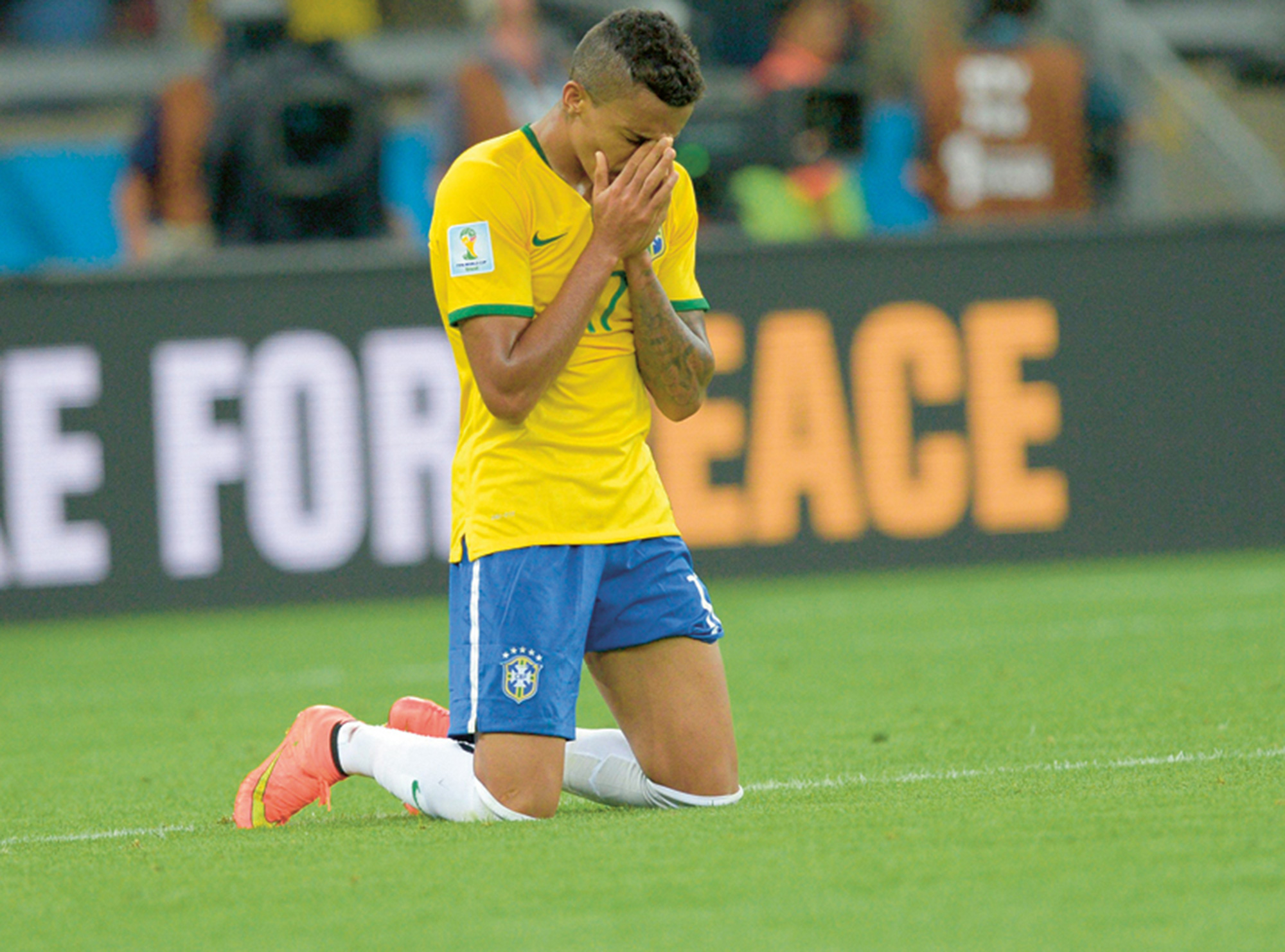 A photograph of a soccer player kneeling on the pitch with his hands in prayer.