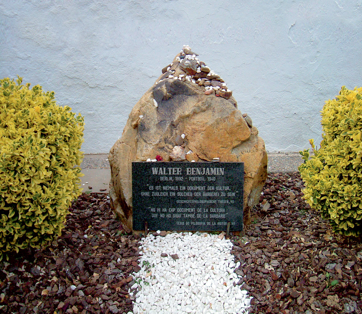 A photograph of Walter Benjamin’s grave in Portbou, Catalonia, where he committed suicide in September nineteen forty. The epitaph, in German and in Catalan, is from Benjamin’s “Theses on the Philosophy of History”: and reads “There is no document of civilization which is not at the same time a document of barbarism.”