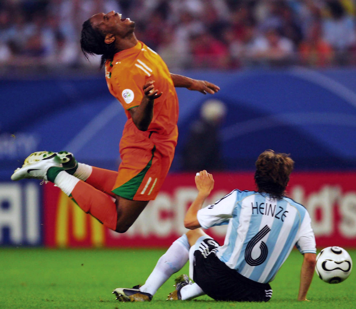A photograph of the Ivory Coast’s Didier Drogba demonstrating a classic “archer’s bow” as he is tackled by Argentina’s Gabriel Heinze in the two thousand and six World Cup. 