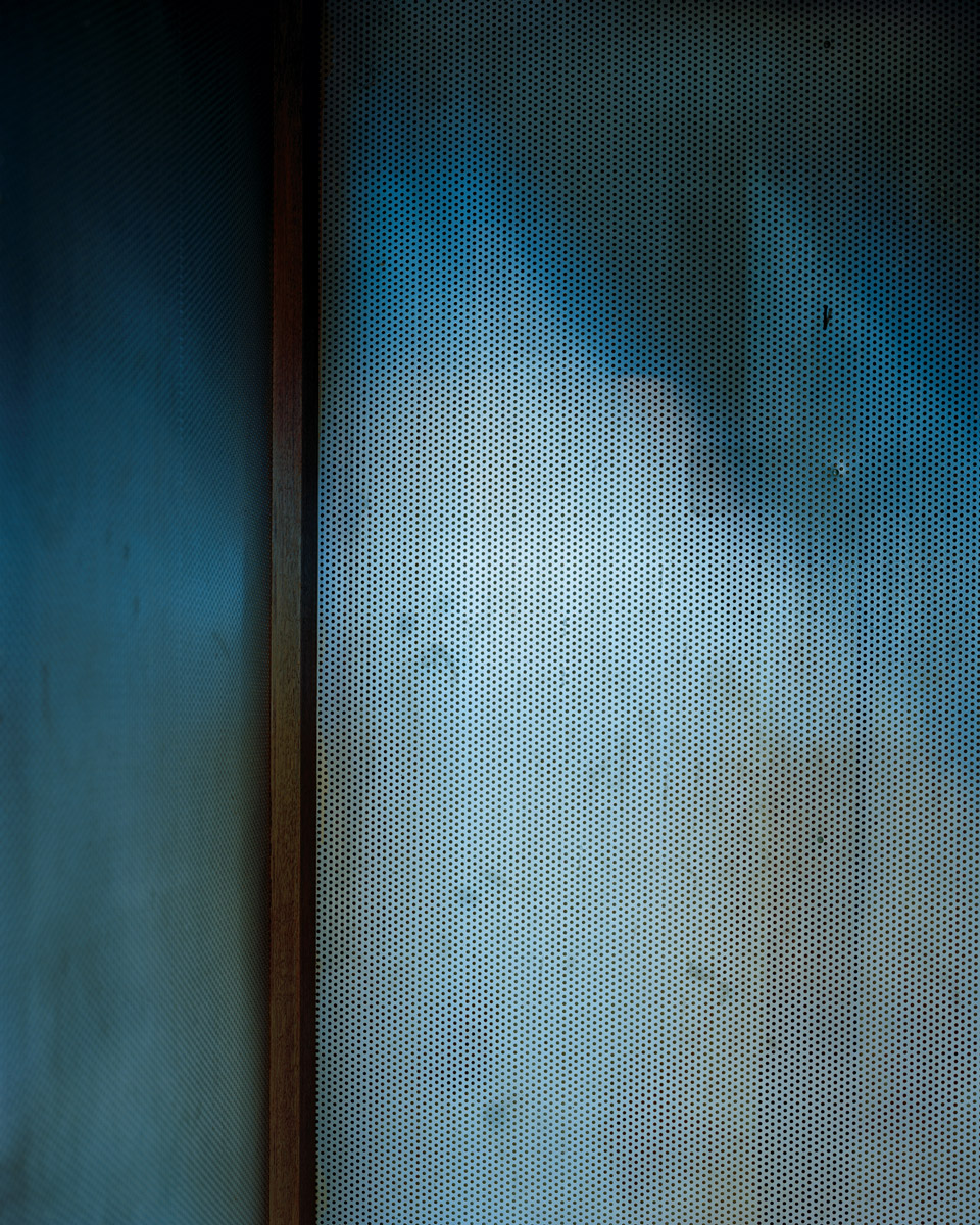A photograph of the inside of a confessional booth, with a blue wall marked by stains and wear, which the artist associates with Saint Peter.