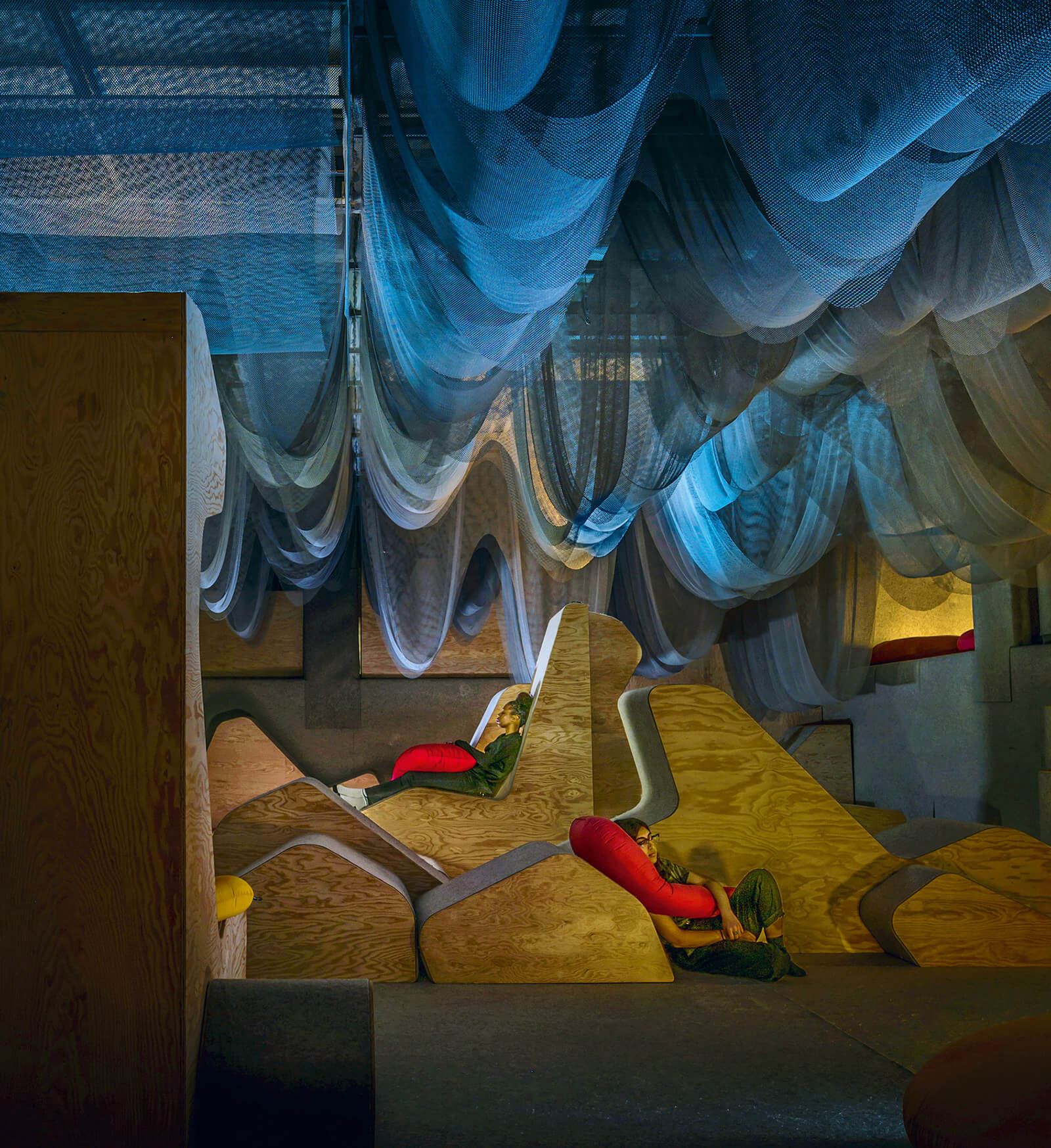 A photograph of two people in “New Circadia,” an experimental space by Richard Sommer and Pillow Culture (Natalie Fizer and Emily Stevenson), at the Architecture and Design Gallery, University of Toronto, twenty nineteen to twenty twenty.