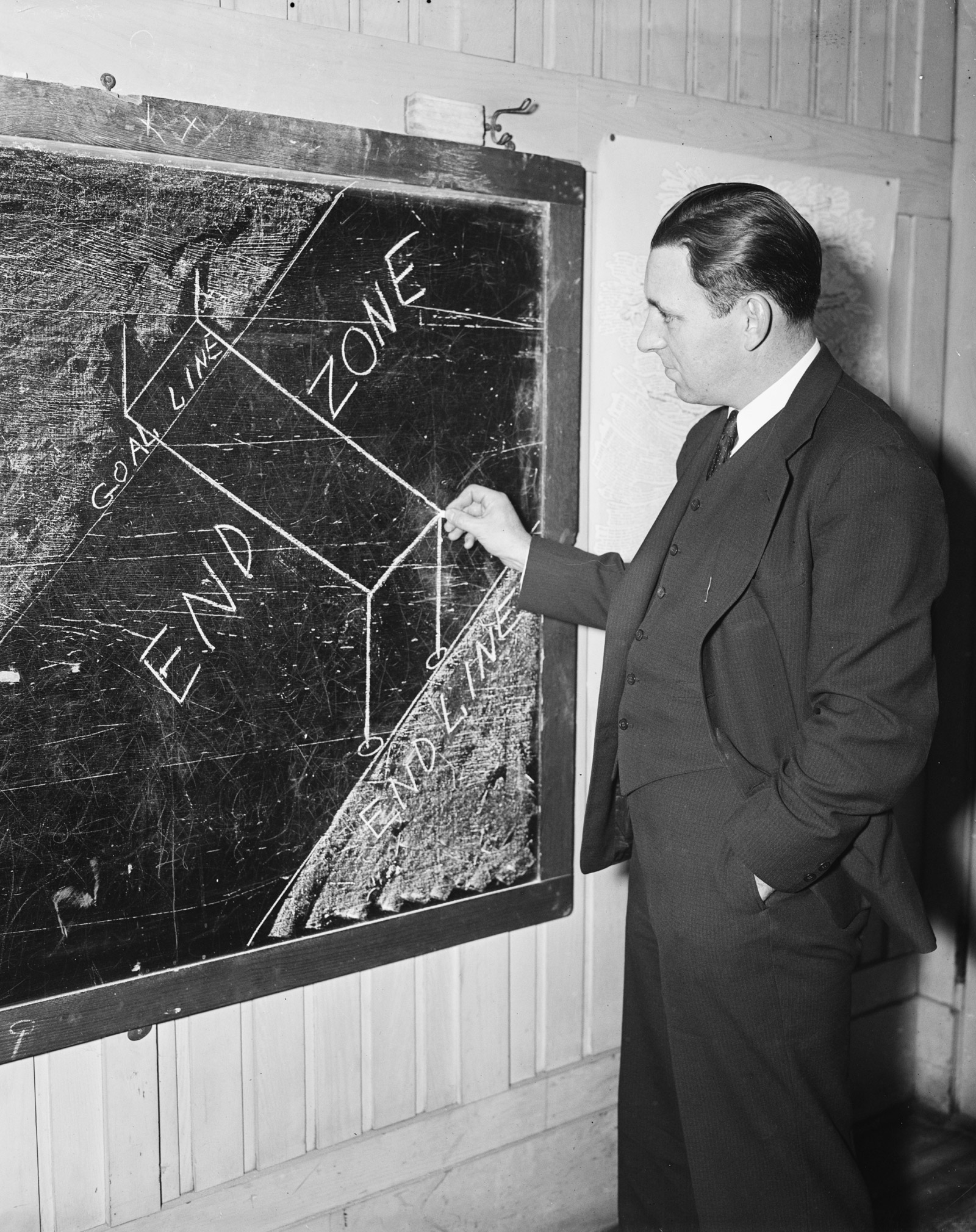 An undated nineteen thirty-six photograph of an American football expert drawing an end zone with his last bit of chalk.