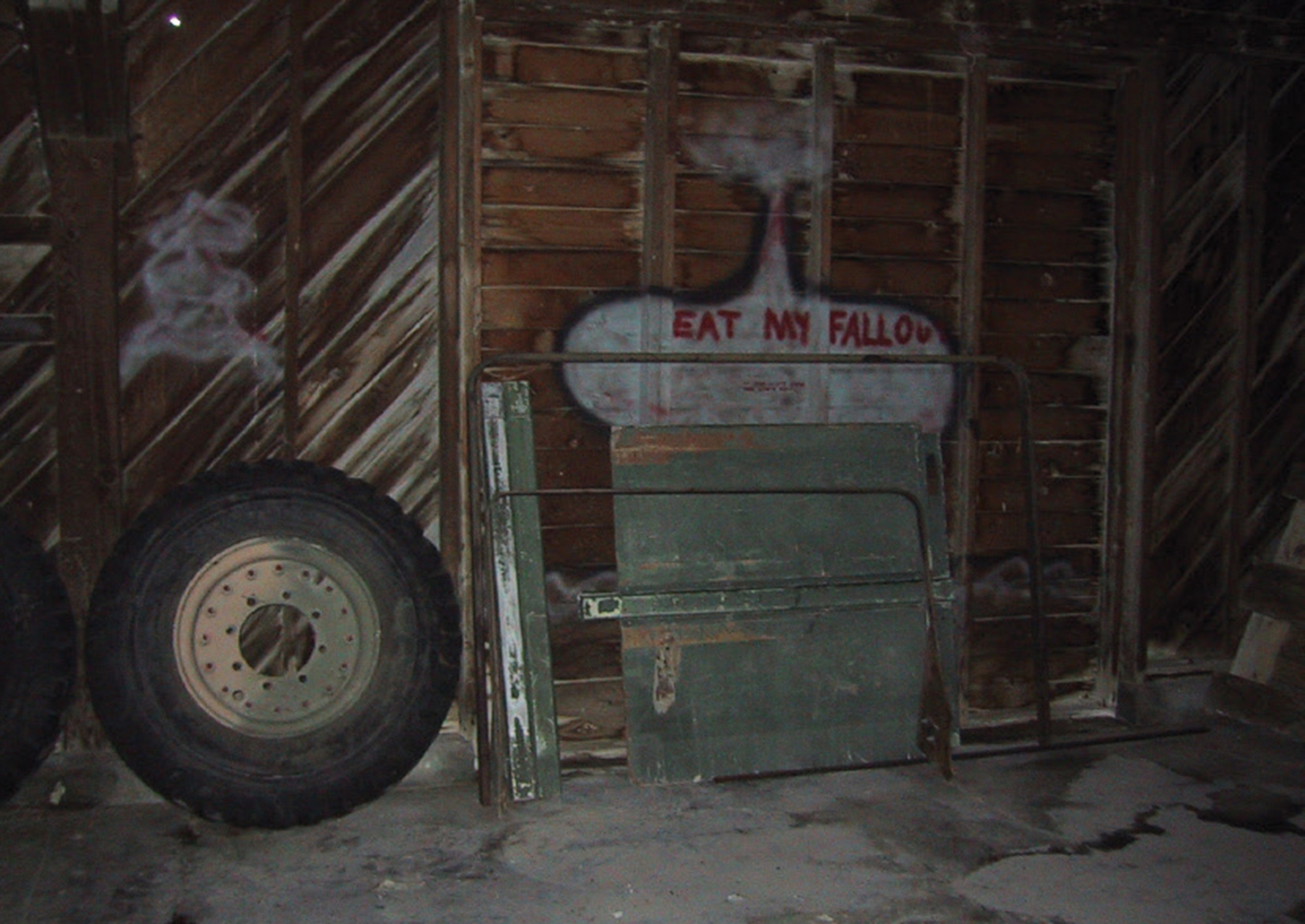 A photograph of graffiti on the inside of a wooden structure reading “Eat my fallout.”