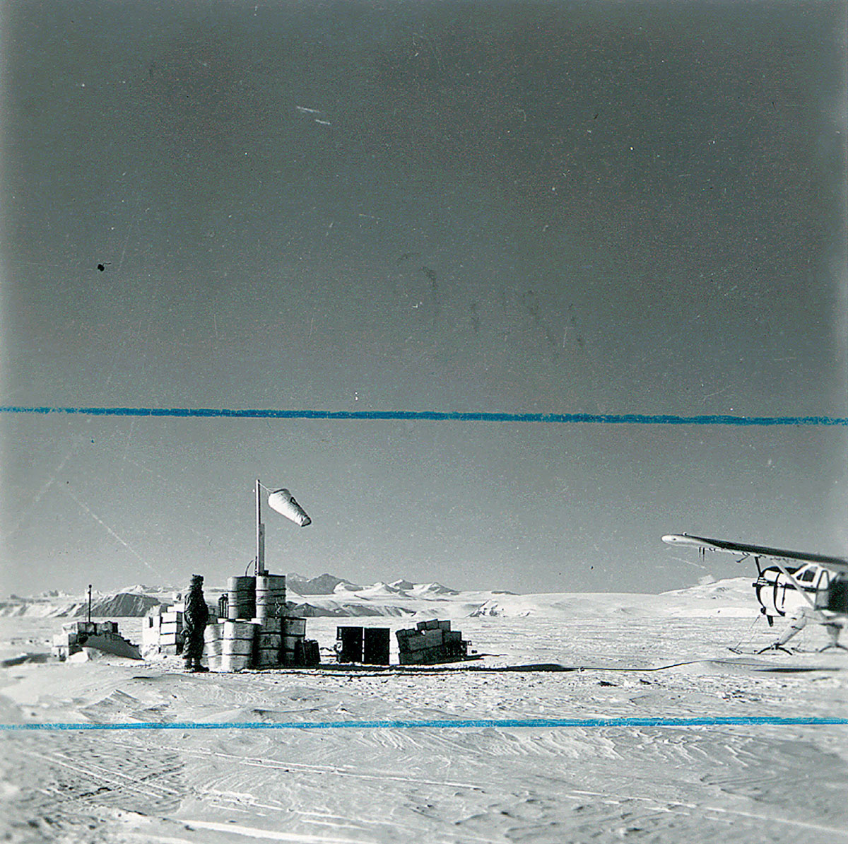 A photograph of an explorer in Antarctica with blue crop marks across the frame.