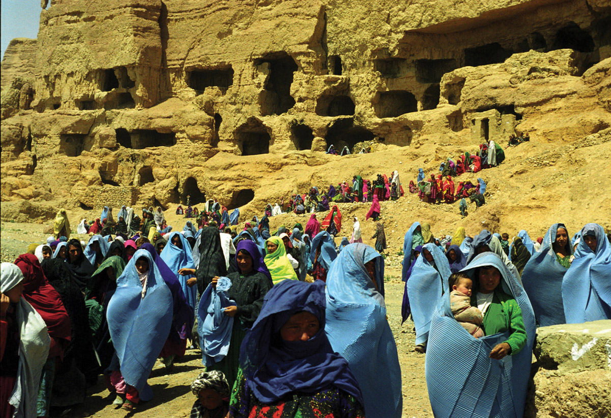 A photograph of women and children walking away from the cliff with the Buddha grottoes.