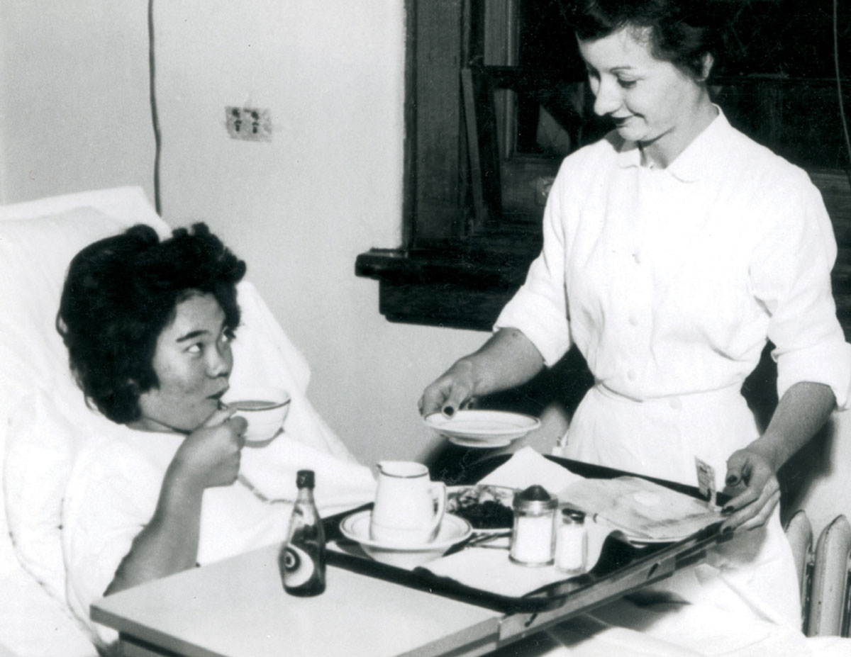 A promotional photograph of a Hiroshima Maiden eating lunch with soy sauce in her hospital bed at Mount Sinai Hospital, New York City, 1955.