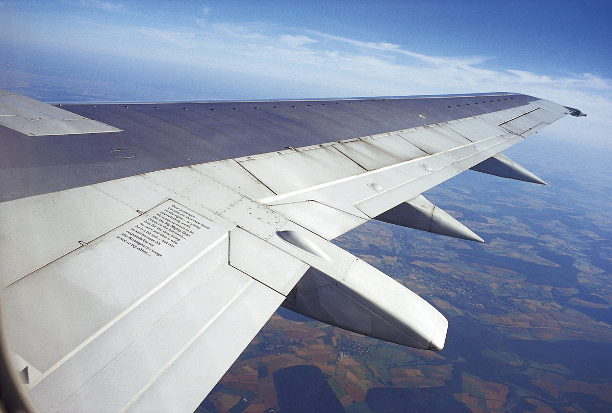 A photograph of an airplane wing with text written on it, pointing out specific clouds.