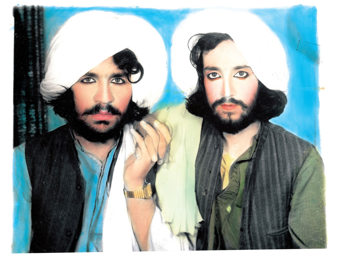 Studio portrait of two Taliban members, holding hands.