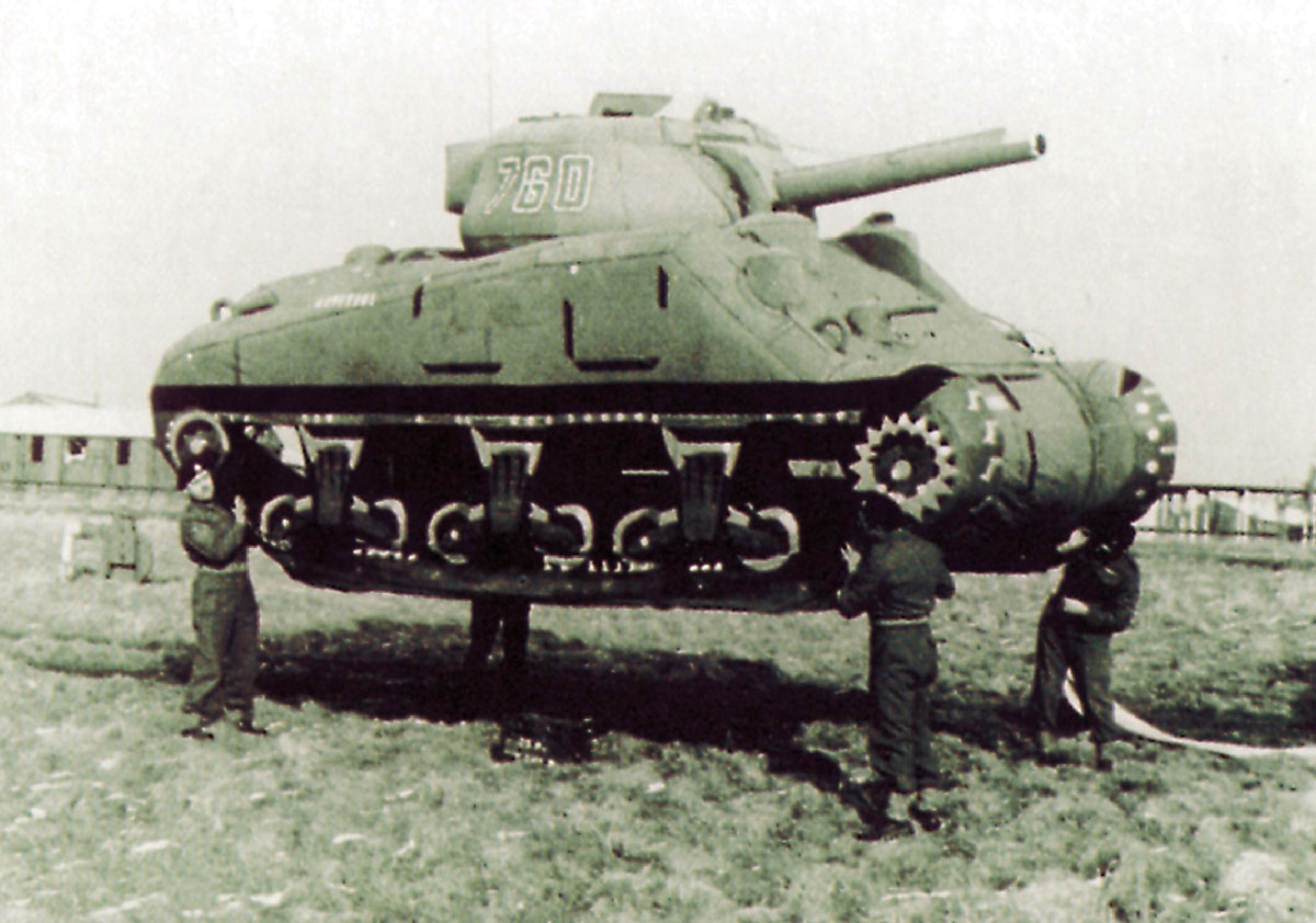 Photograph of four men holding up a World War II-era inflatable tank.