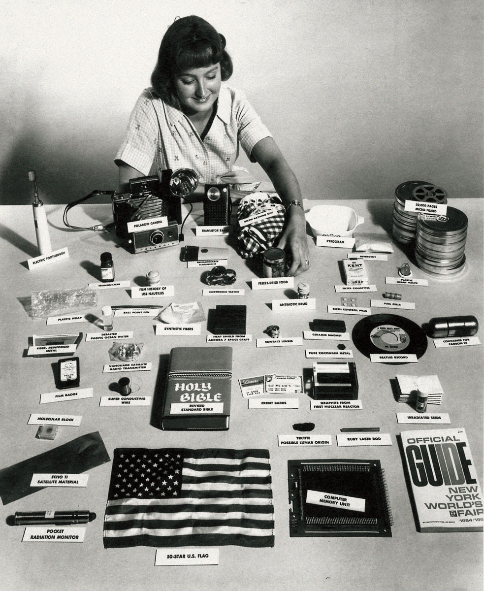 A photograph of a woman at a table displaying labeled miscellaneous objects from the Westinghouse time capsule created for the 1964–1965 New York World’s Fair.