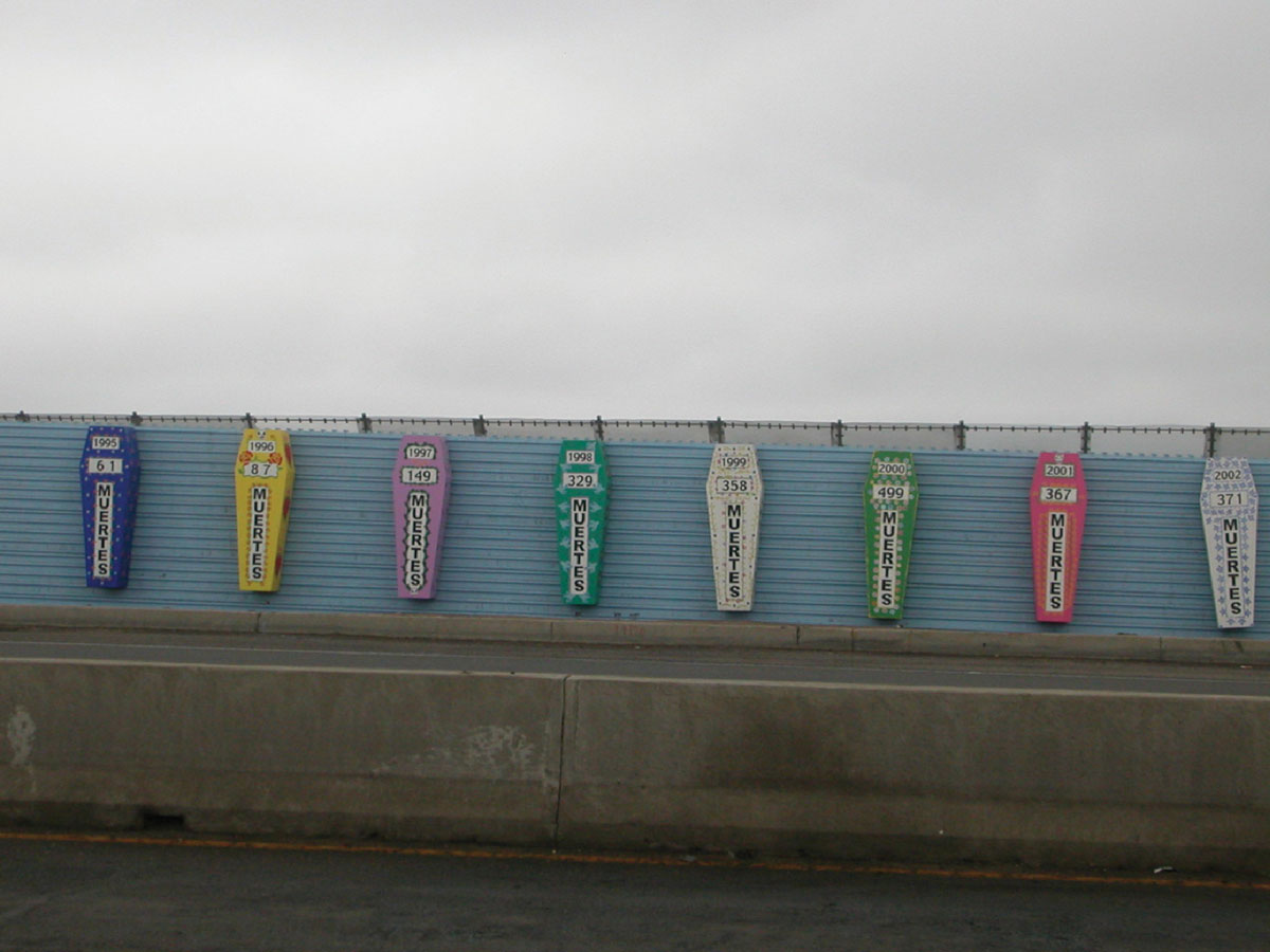 A photograph of brightly painted coffins hanging on a border fence.