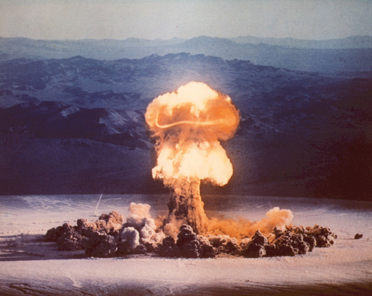 A photograph of a nuclear explosion mushroom cloud with mountains in distant background.