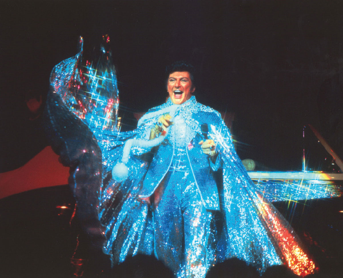 A photograph of Liberace performing in a sequined blue suit and cape.