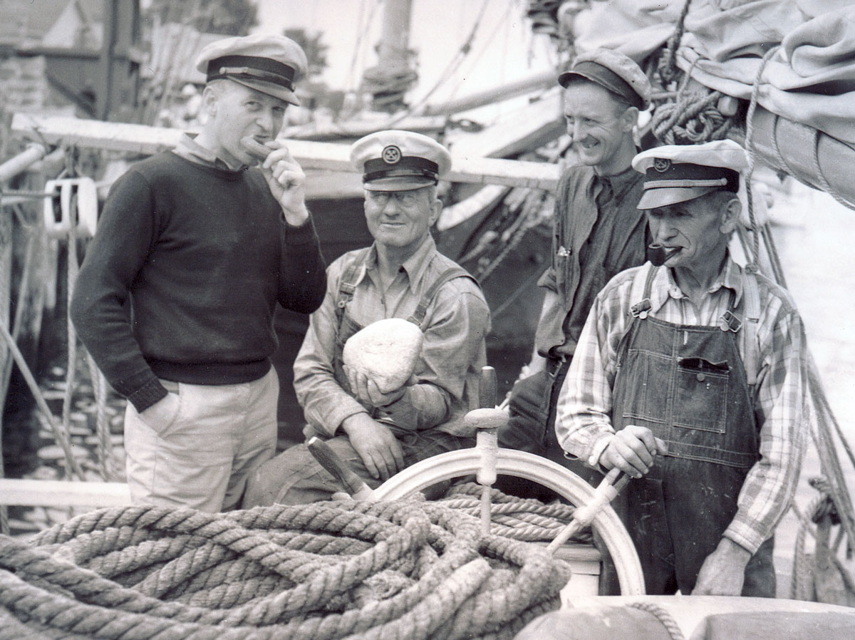 Four men on board with an old doughnut, date unknown. Caption on the back of the photograph reads: “Mistaken for rocks at the bottom of the harbor, it was discovered these large objects were, in fact, old solid doughnuts accidentally dropped overboard from vessels at anchor.” Photo courtesy of Camden Public Library, Camden, Maine.
