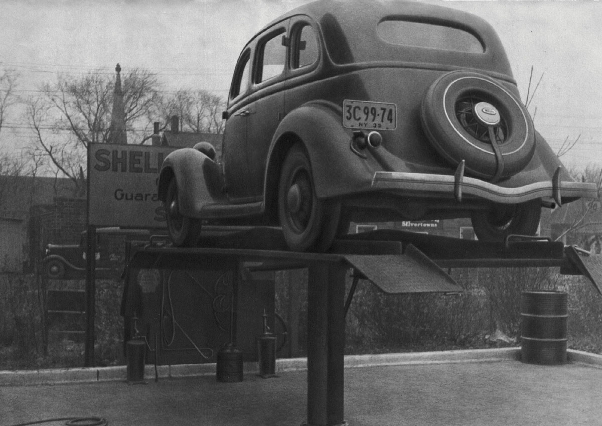 Black-and-white photograph of a car getting an oil change.