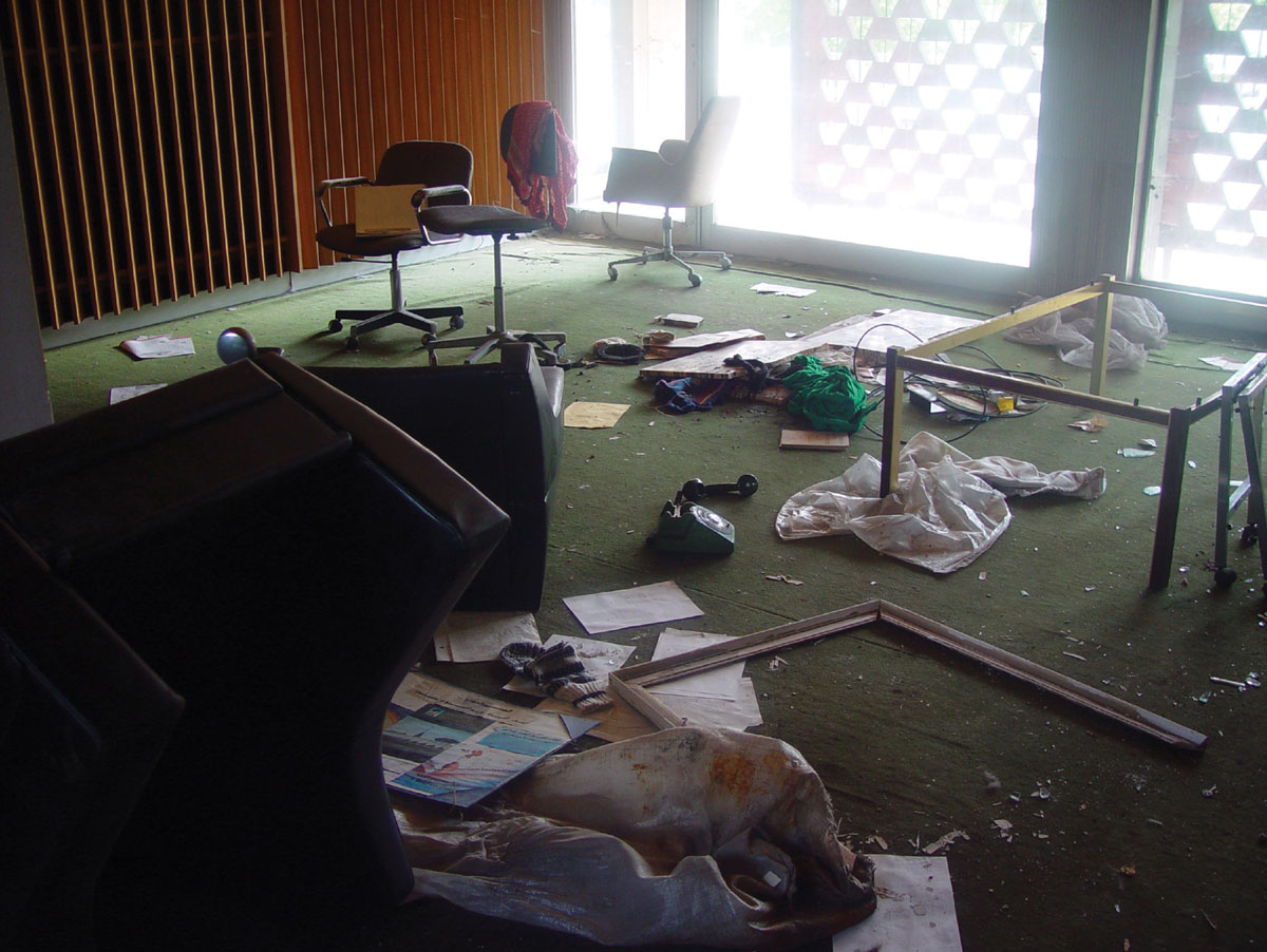 A photograph of a trashed office with chairs, telephone, coffee table.