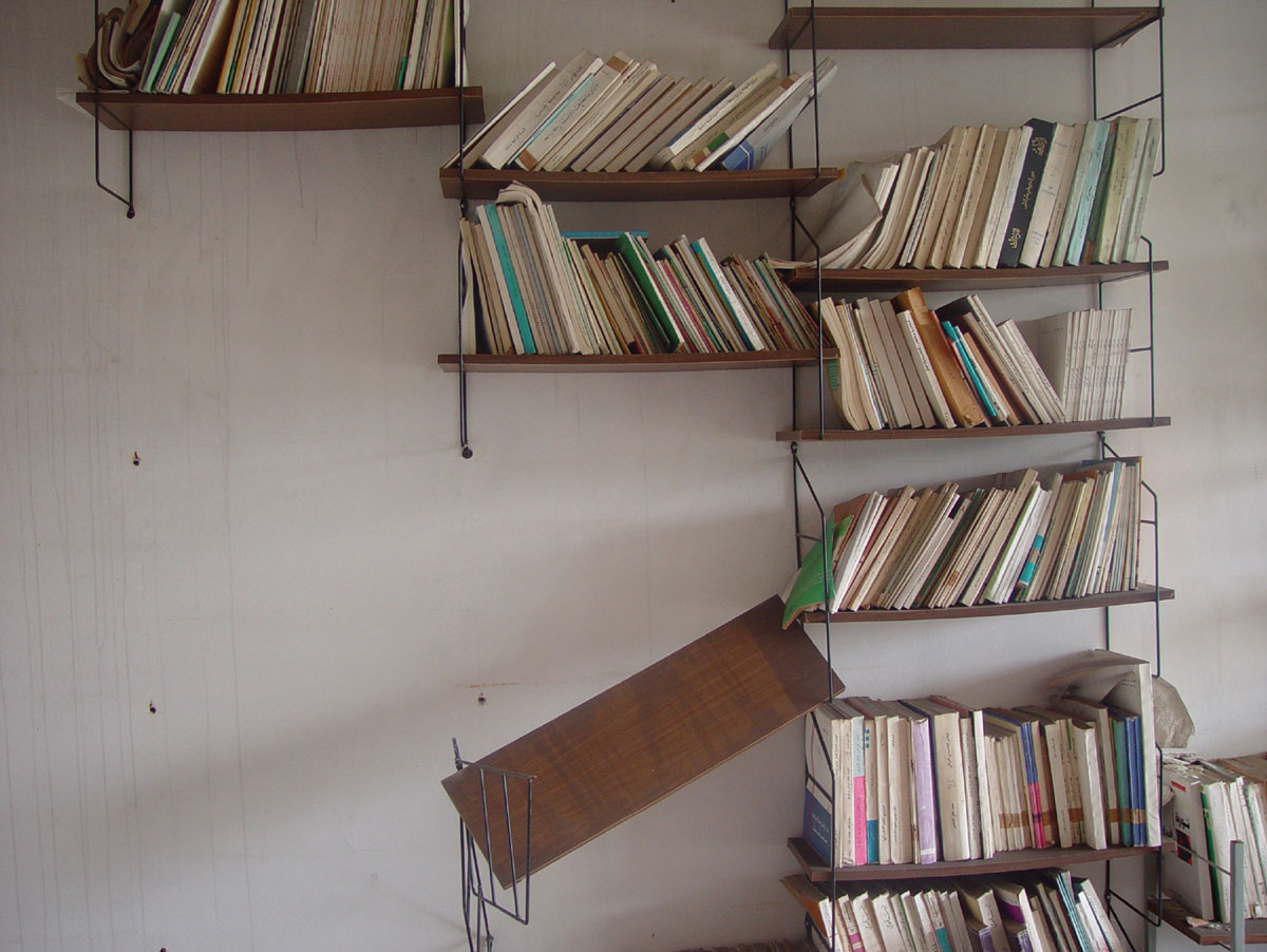 A photograph of wall-mounted bookshelves filled with books except for one shelf hanging off the wall, empty.