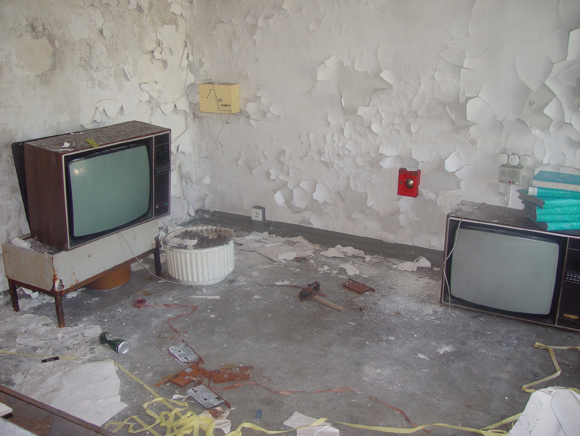 A photograph of paint peeling off the walls in a room where a small television sits on the ground.