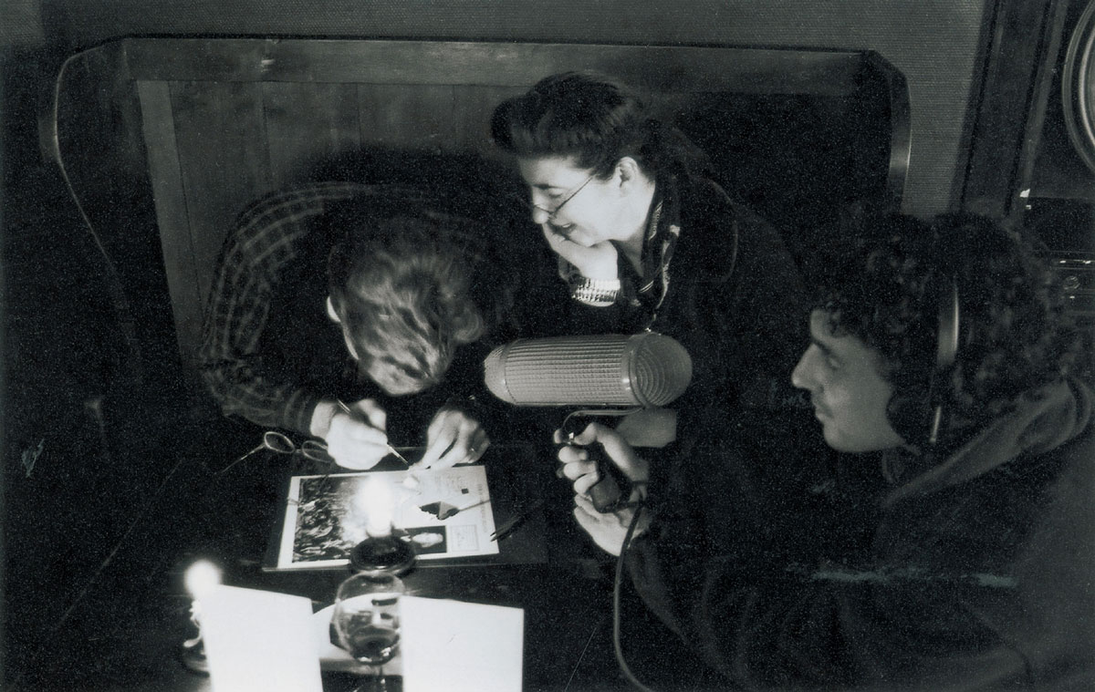 A photograph of three figures crowded around a table inspecting a small object.