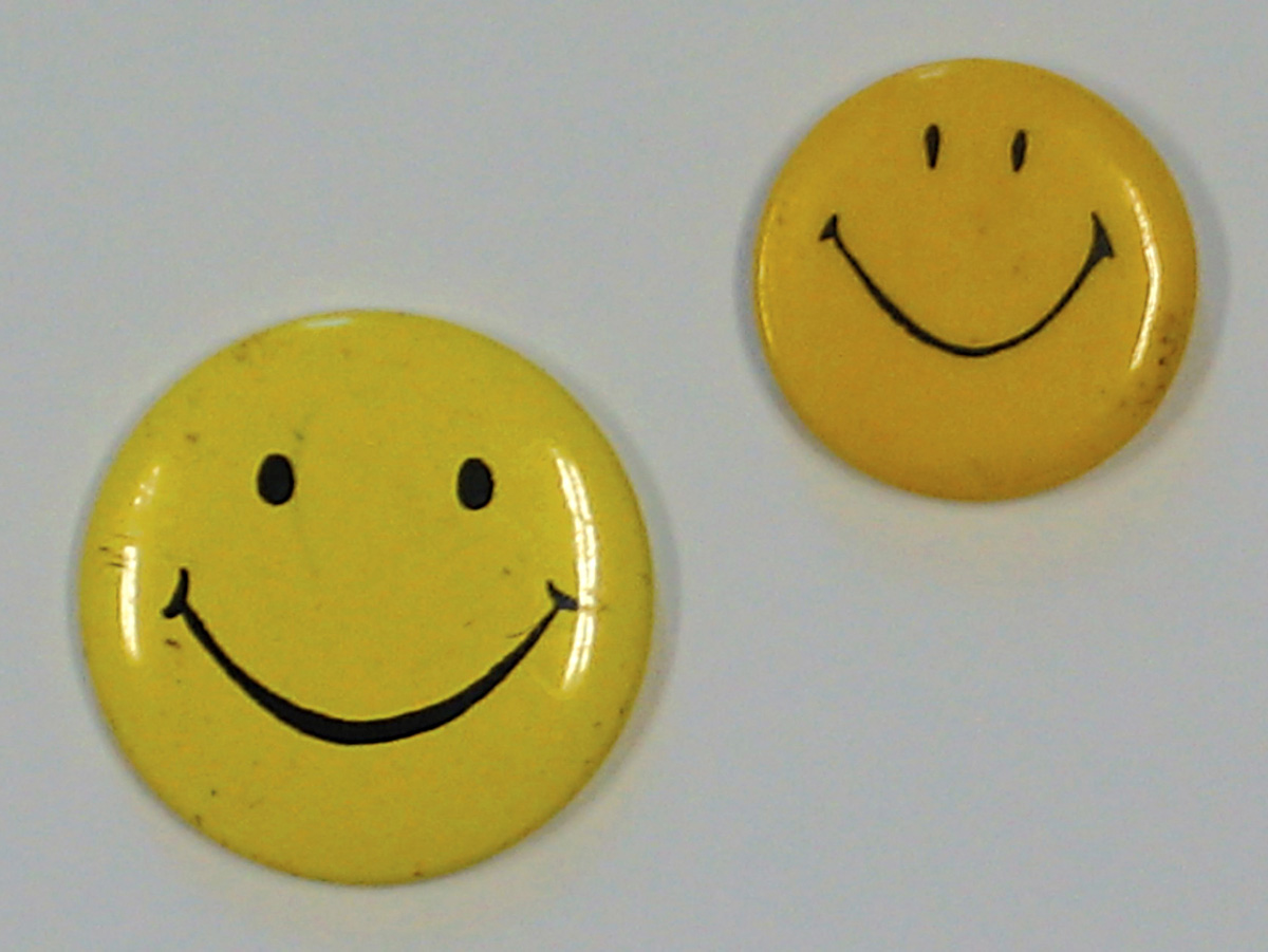 A photograph of two vintage smiley buttons.