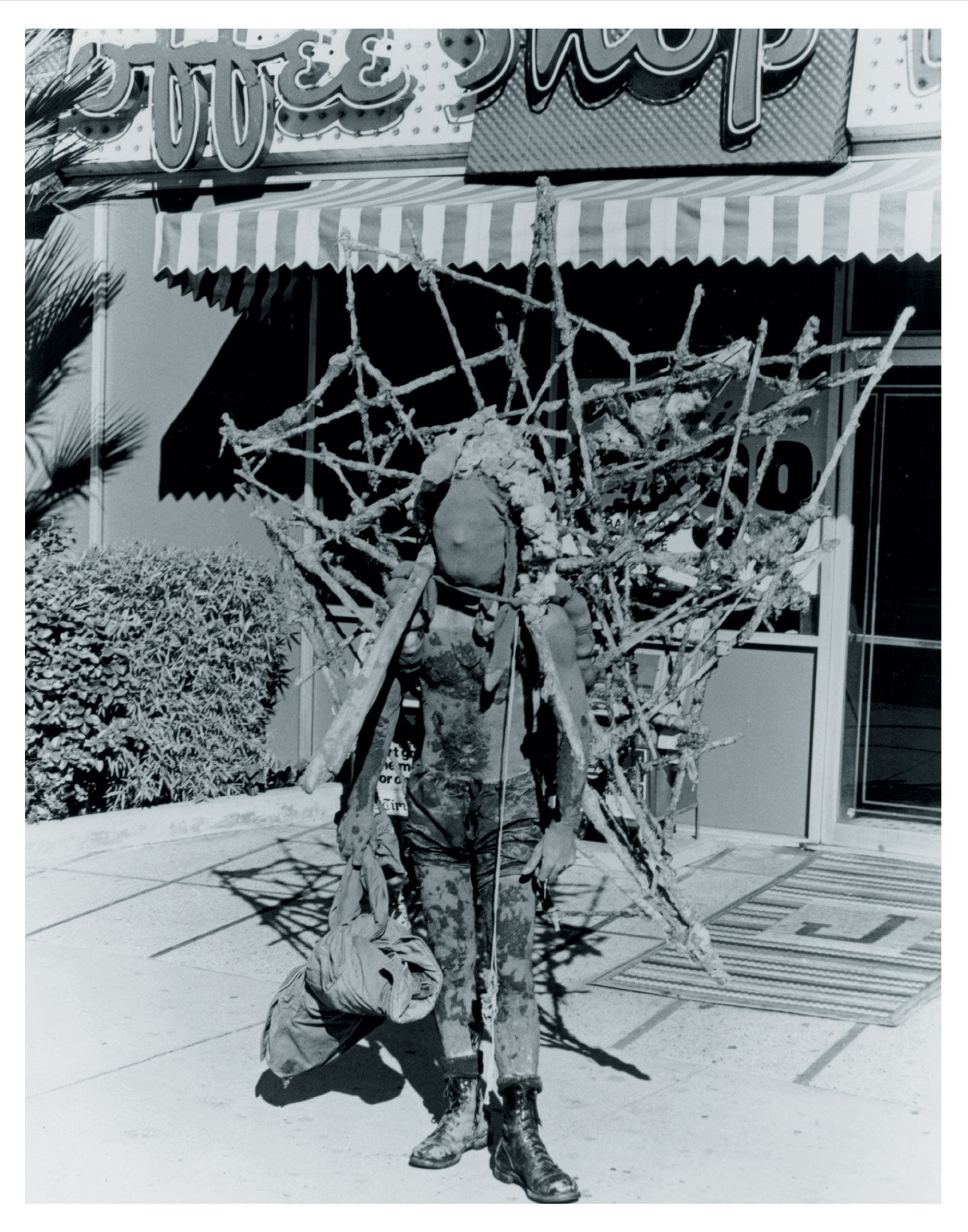 A postcard project by artist Kim Jones featuring a 1976 photograph of him as the Mudman performing his “Wilshire Boulevard Walk,” which went from Los Angeles to Santa Monica on 28 January 1976.