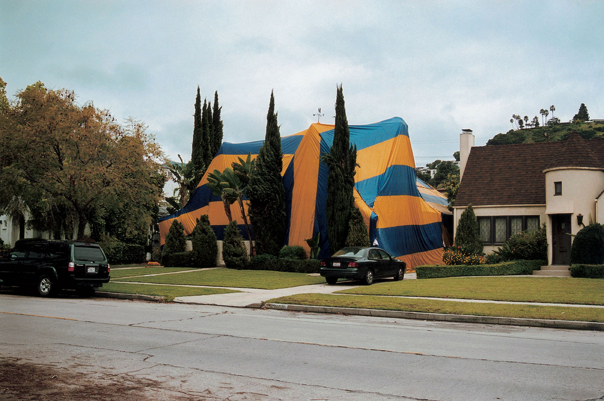 Artist Susan Silton’s photograph of a house enveloped in striped tarpaulin.