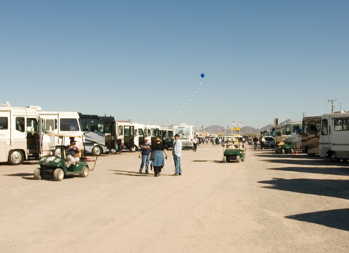 A photograph of people standing on a dirt road between long rows of RVs in Quartzsite.
