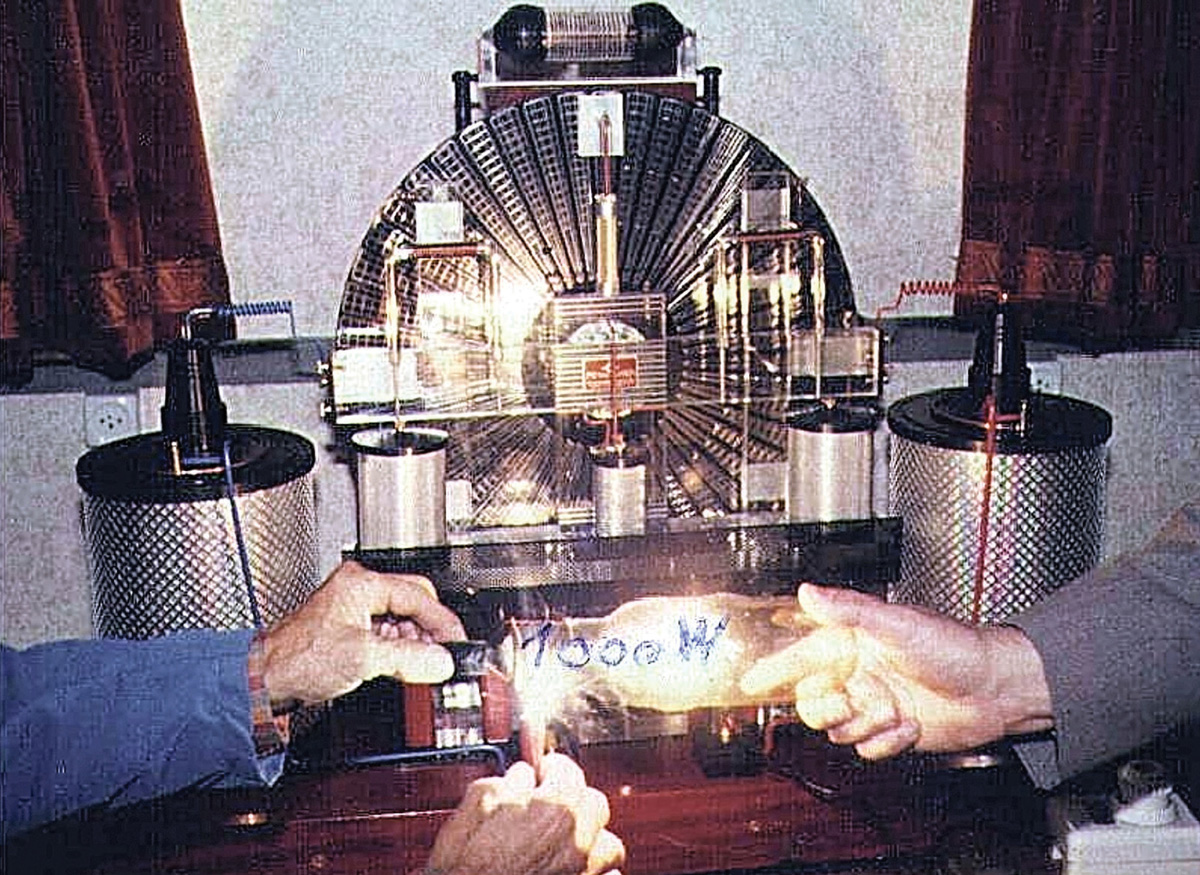 A still photograph, with handwriting on it, taken from an eight millimeter film of the Testatika, which is shown powering a thousand watt bulb. The hands of the free-energy machine’s inventor, Paul Baumann, are visible on the left.