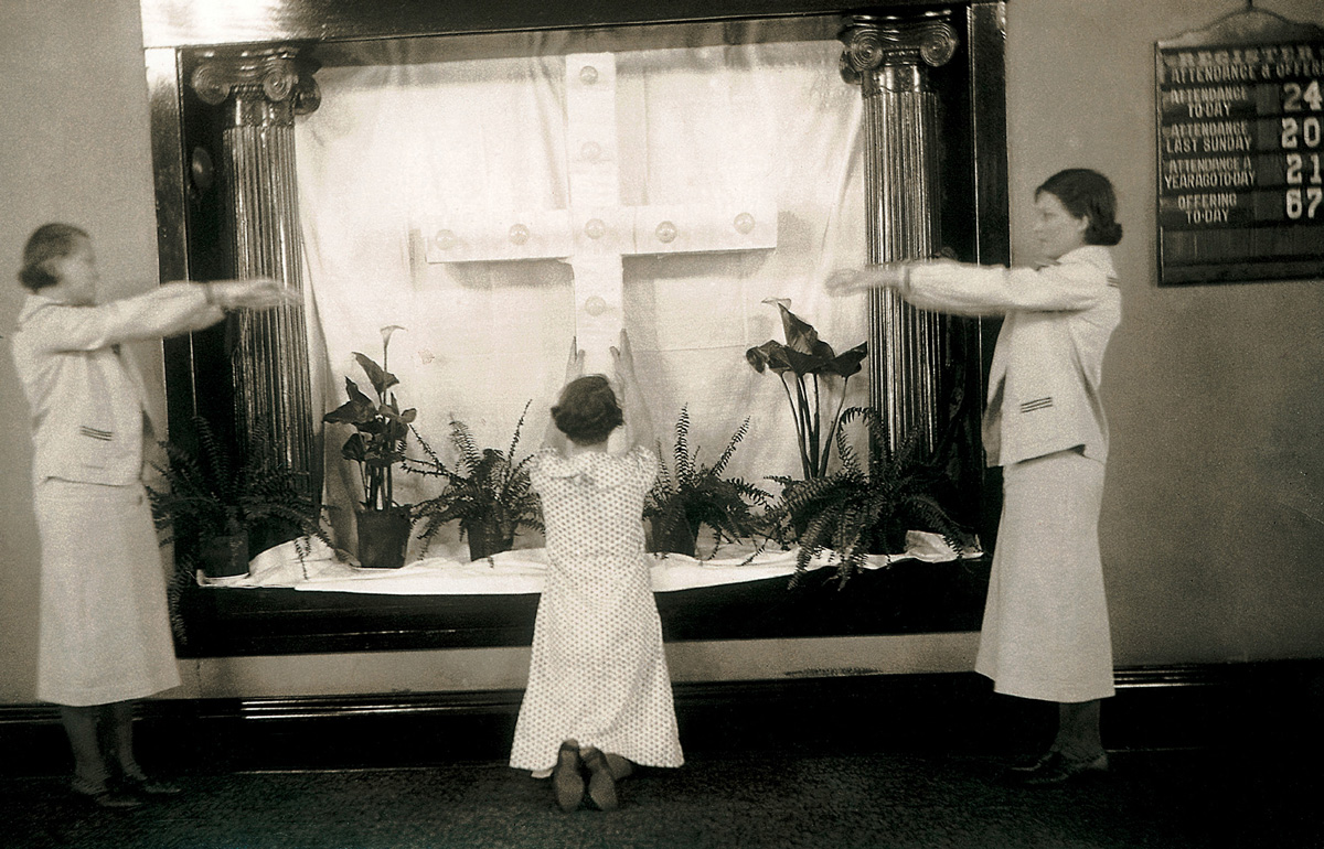 A photograph showing three women miming “Rock of Ages” in front of a makeshift altar with a cross decorated with light bulbs, Easter nineteen thirty five.