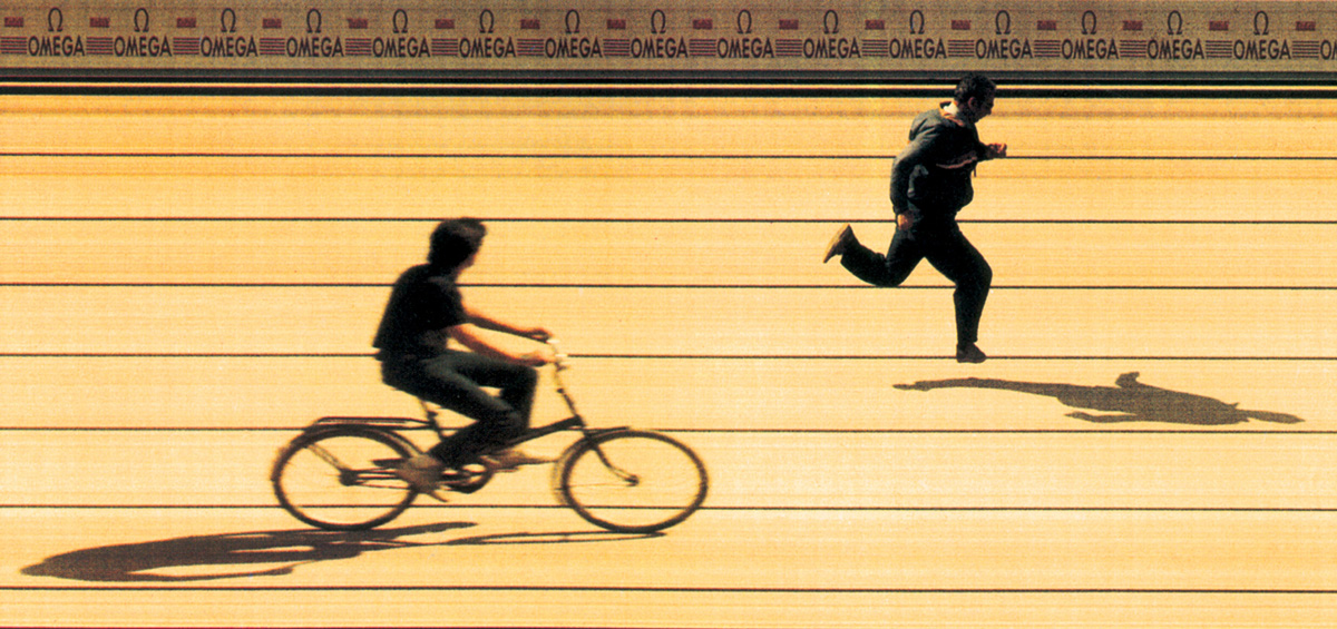 A photo-finish camera records an object moving past its exposure slit over time. The resulting images often capture information in a manner surprisingly different from that of a conventional camera. For instance, in this strip photograph the biker and runner crossed the finish line moving in opposite directions—the runner from left to right, and the cyclist from right to left. Strip photography, however, builds up the image of passing objects in the direction that the film itself moves inside the camera, in this case from left to right. Thus, the direction of the cyclist has been reversed. The paradoxical orientation of the two shadows remains the only clue to the reversal because the shadows have kept their original relationship with respect to the objects that cast them.