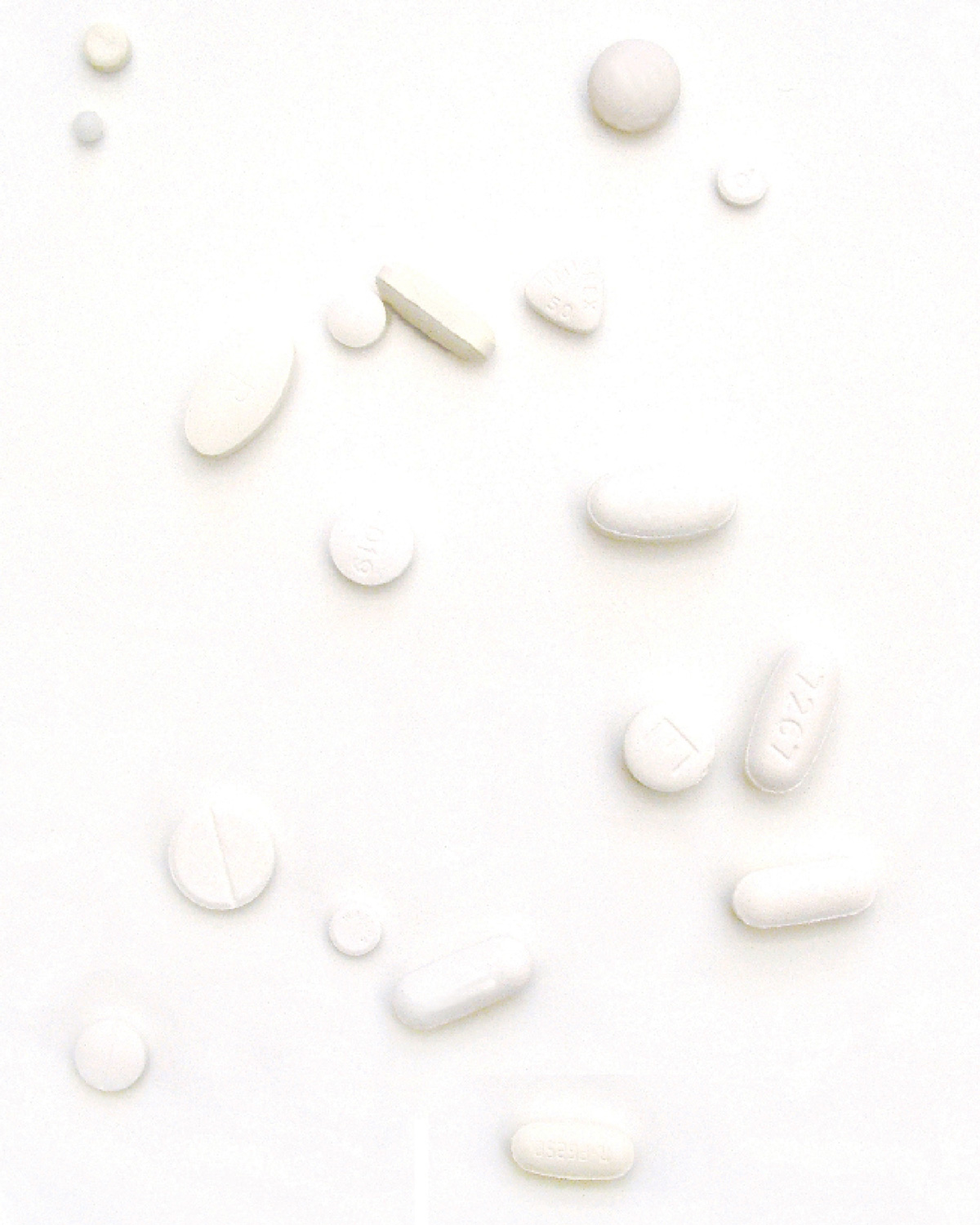 A photograph of a number of different white pills on a white background.