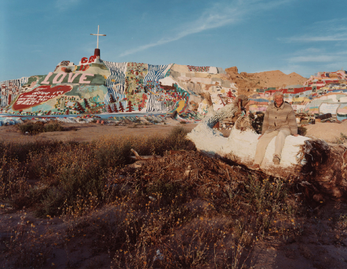 A photograph by artist Joel Sternfeld titled “Leonard Knight at Salvation Mountain, Slab City, California, March two thousand and five,” two thousand five. Courtesy the artist and Luhring Augustine Gallery.