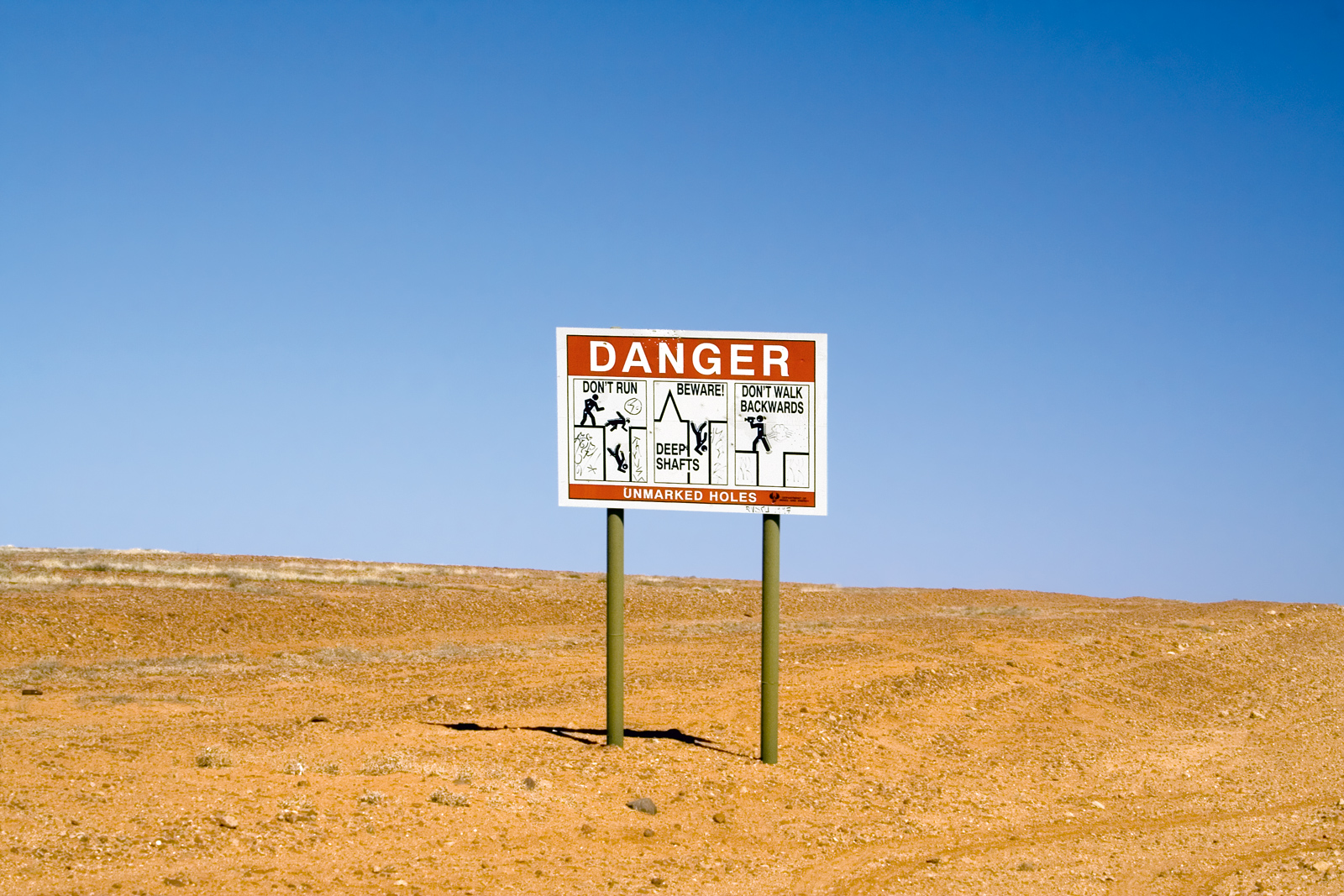 A photograph of a warning sign on the outskirts of Coober Pedy, an opal-mining town in South Australia where excessive heat leads townspeople to build their homes in hillside caves. The advantage of underground living is diminished somewhat by the danger of falling.