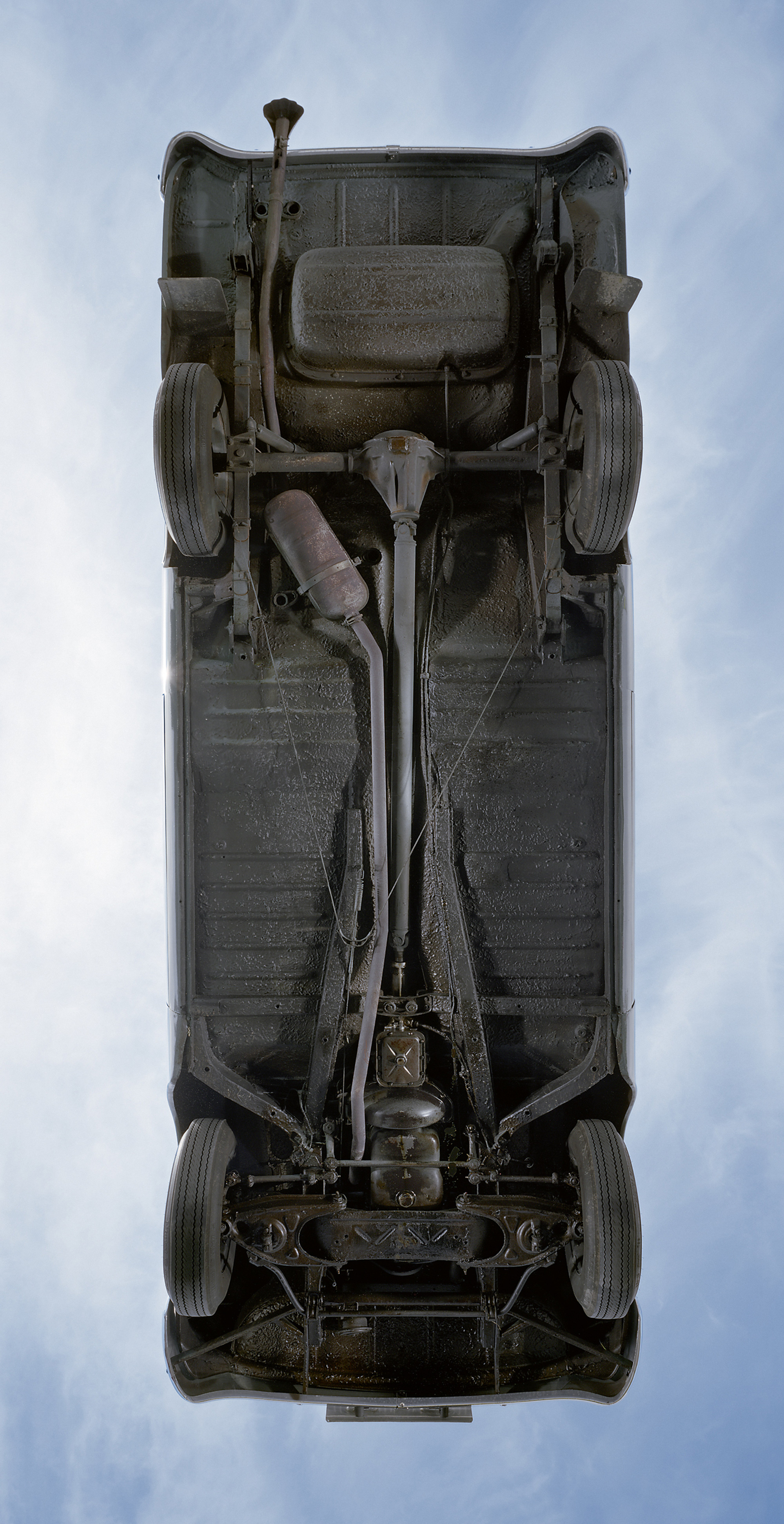 A photograph of the underbelly of a car resting on a large sheet of heavy-duty glass.