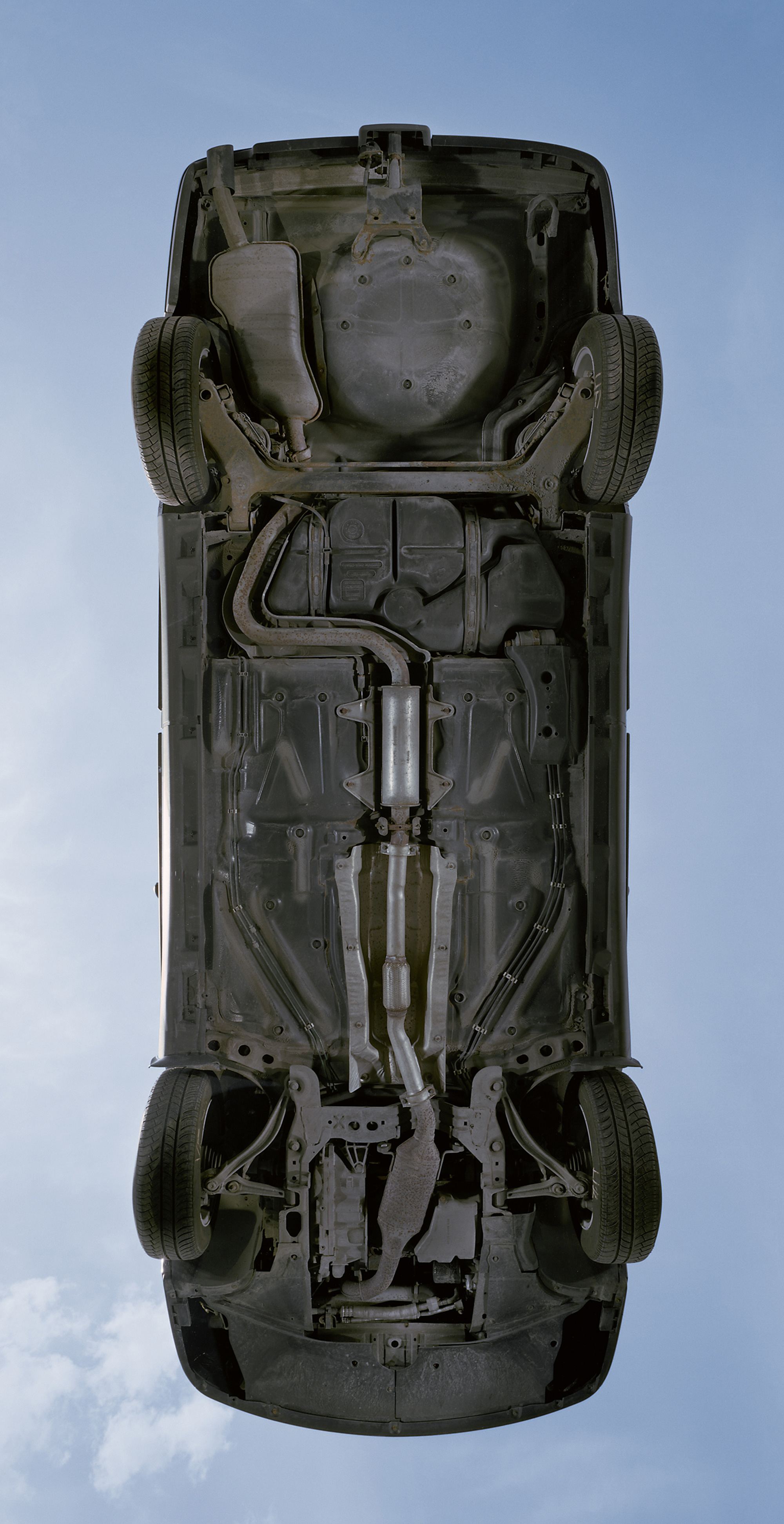 A photograph of the underbelly of a car resting on a large sheet of heavy-duty glass. 