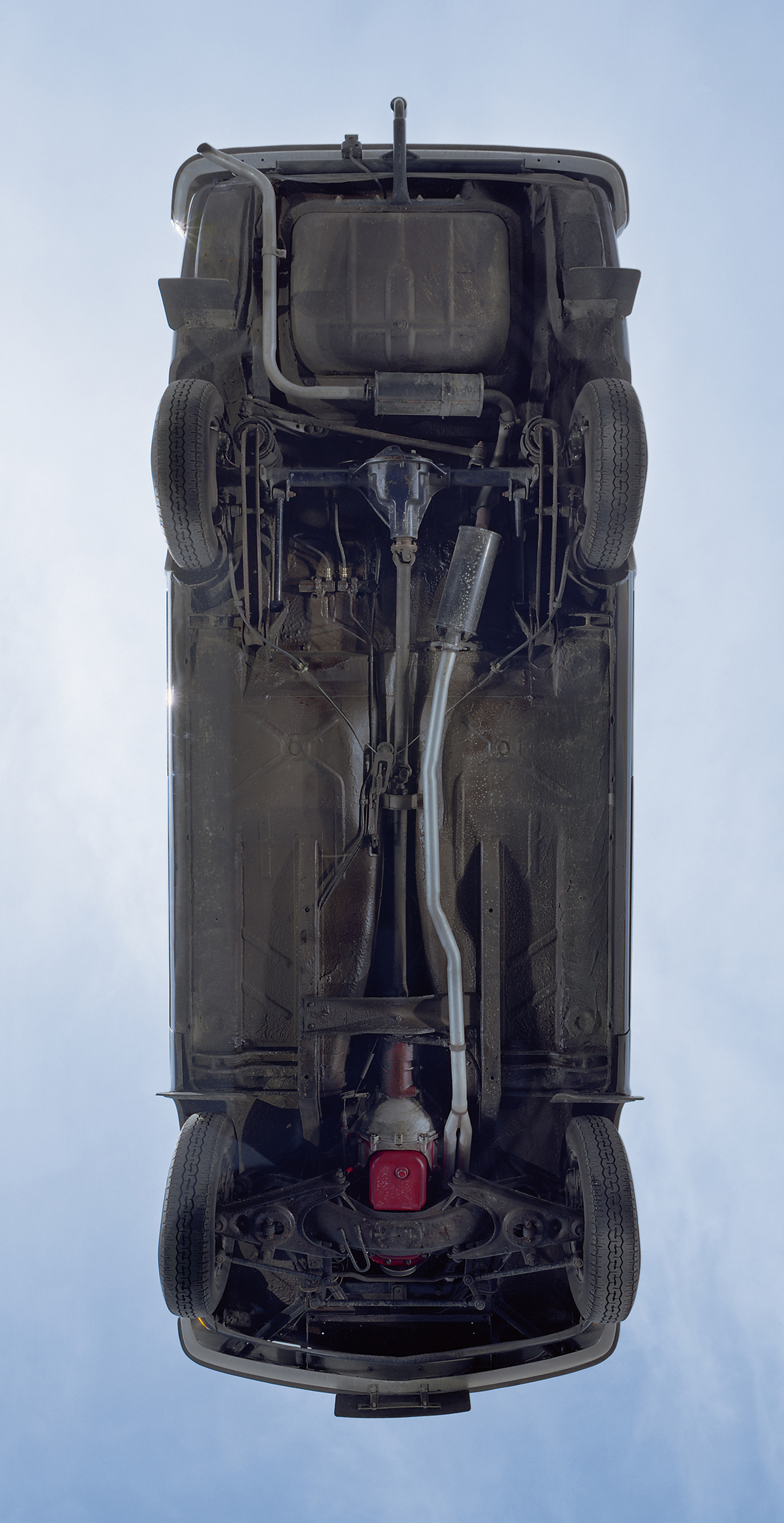 A photograph of the underbelly of a car resting on a large sheet of heavy-duty glass.