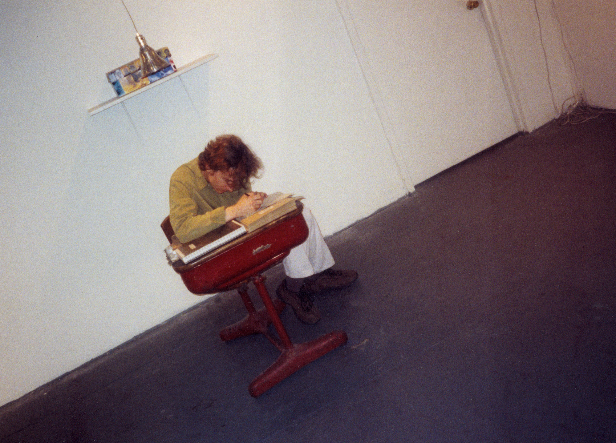 A color photograph, shot at a Dutch angle, of a man writing on a red desk.