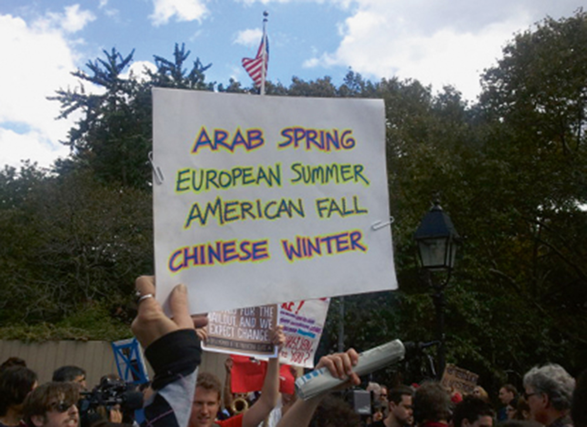 A twenty eleven photograph of a protest sign that reads “Arab Spring, European Summer, American Fall, Chinese Winter.”