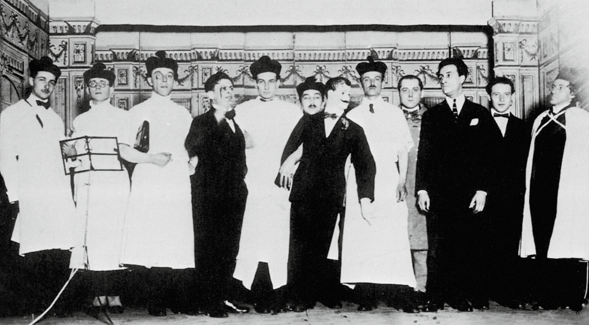 A photograph of eleven angry men at the nineteen twenty-one trial. Left To Right: Louis Aragon, Pierre Deval, André Breton, Tristan Tzara, Philippe Soupault, Théodore Fraenkel, “Maurice Barrès,” Georges Ribemont-Dessaignes, Benjamin Péret, Jacques Rigaut, René Hilsum, Serge Charchoune.