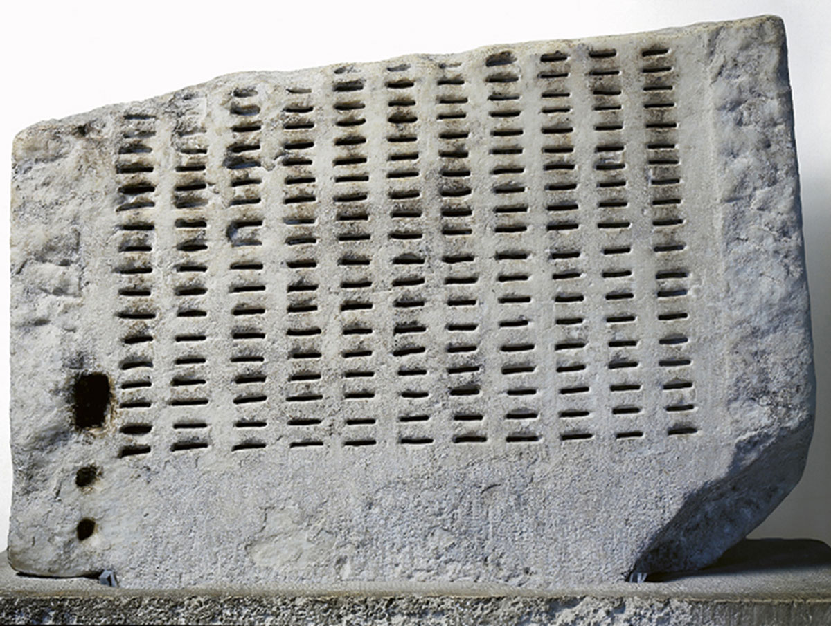 A photograph of a fragment of an allotment device (or, kleroterion) used for random jury selection in third century bee see Greece. A number of black and white balls were dropped into a funnel and the order in which they exited an attached tube determined which horizontal row of potential jurors would serve in a given trial.