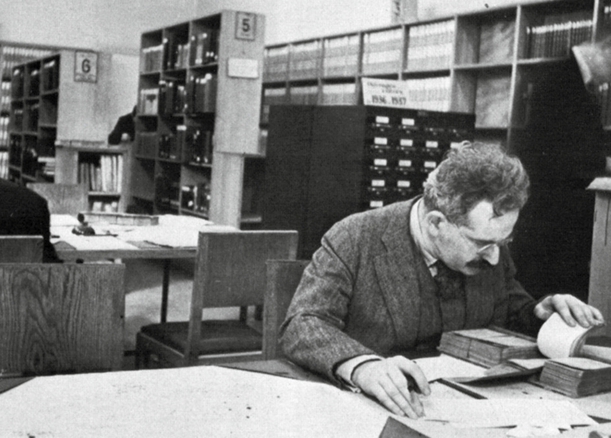 A photograph of Walter Benjamin studying note cards in a library. 