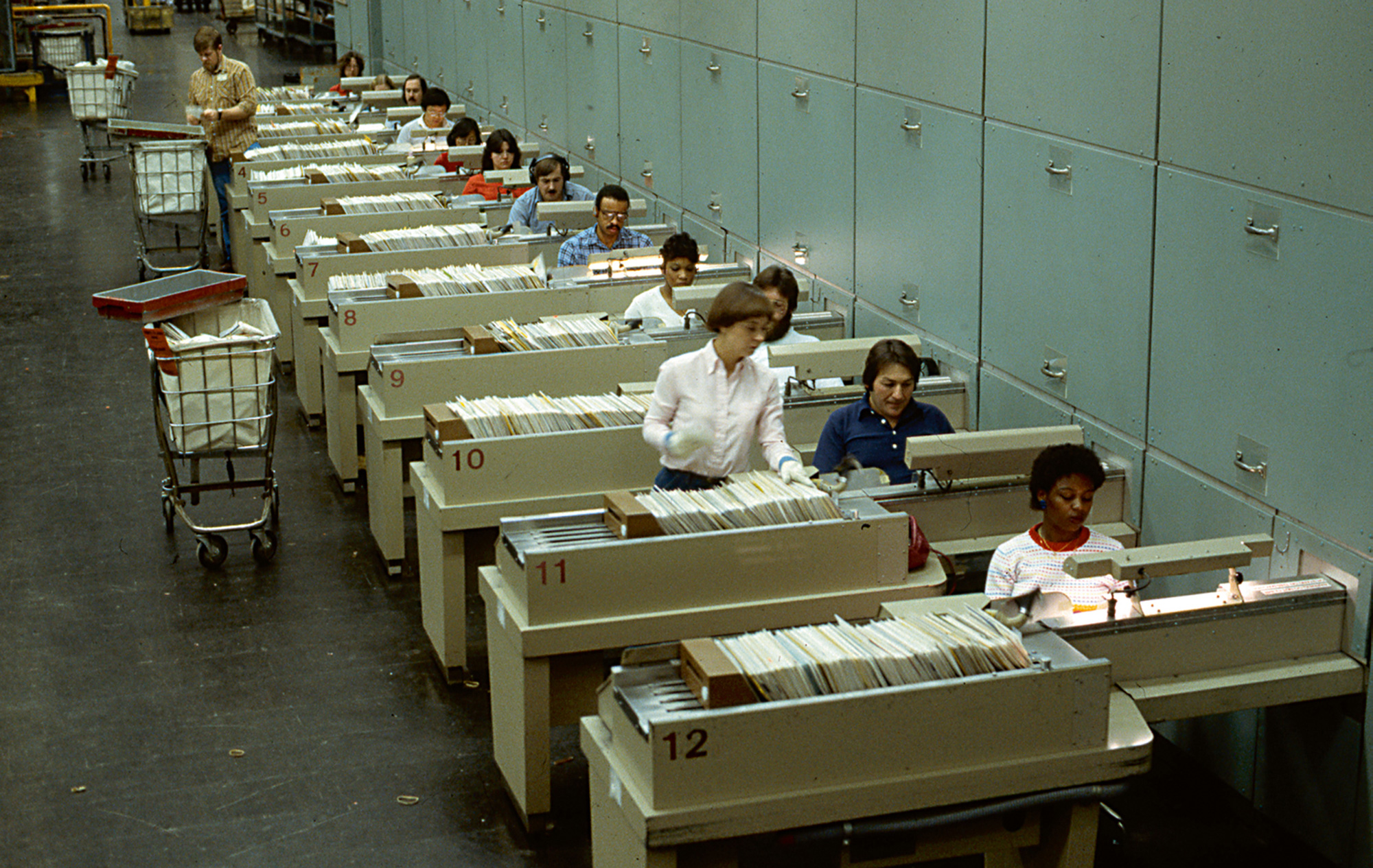 Postal employees at Multi-Position Letter Sorting Machines processing envelopes using the zip code on each, 1970s.