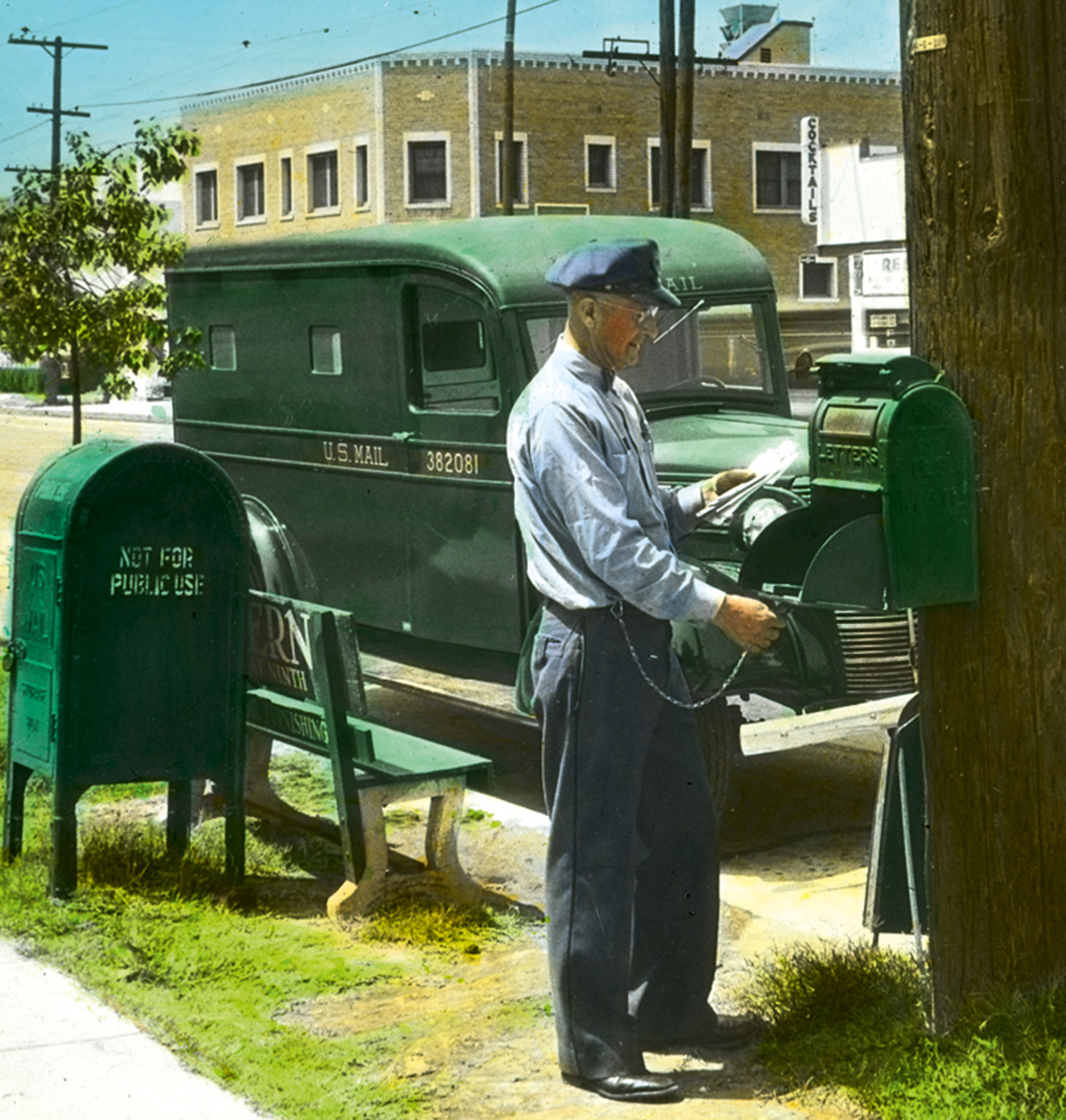 A letter carrier unlocks a mailbox mounted to a telephone pole, ca. 1947.