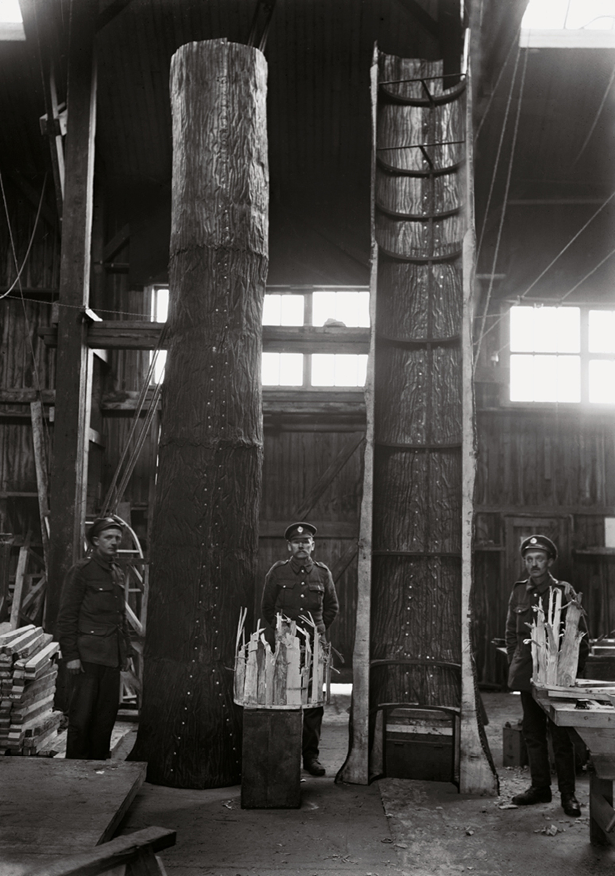 A circa nineteen sixteen photograph of British Royal Engineers posing beside an unfinished camouflage tree.