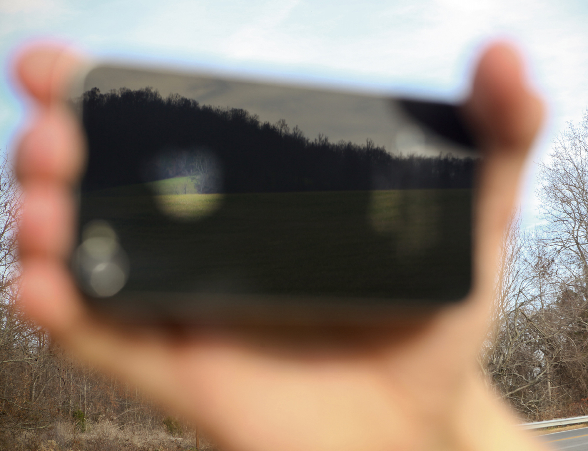A blurred photograph of the back of an IPhone reflecting a landscape. 