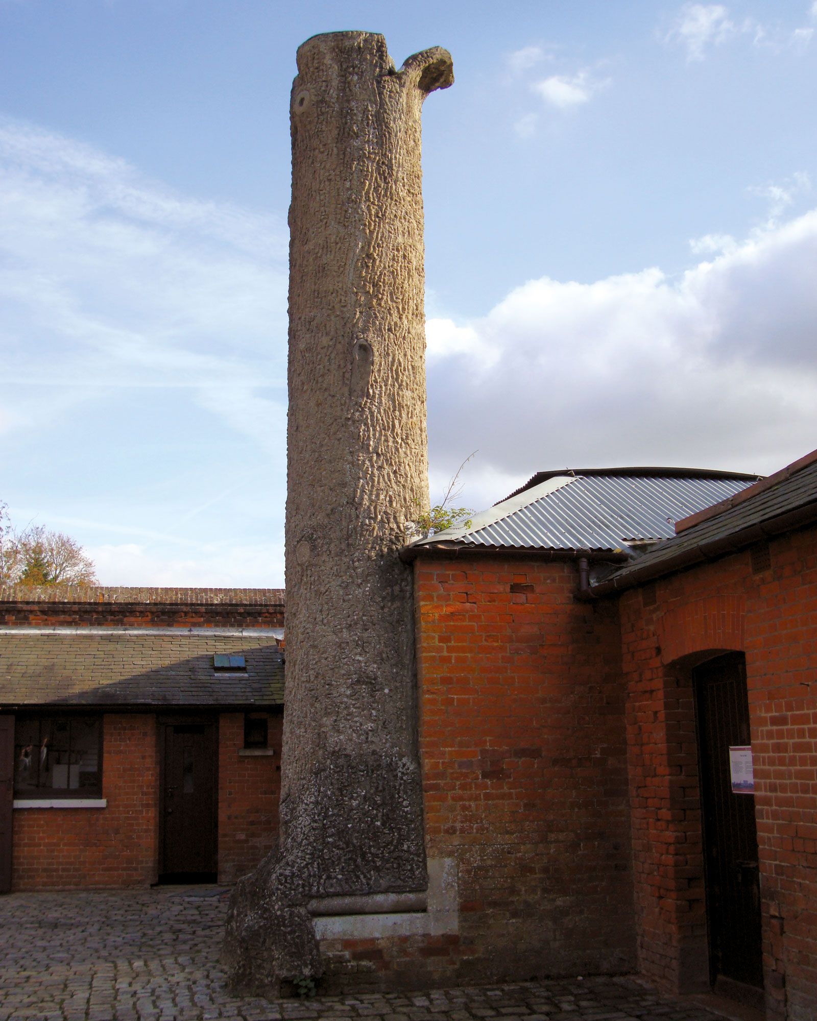 A photograph of a chimney disguised as a tree stump. The caption reads “By the nineteenth century, British country estates frequently used on-site gasworks, rather than oil lamps or candles, to illuminate their rooms. One such system was in place at Cliveden, the sprawling mansion in Buckinghamshire built in eighteen fifty-two and purchased in eighteen ninety-three by the American millionaire William Waldorf Astor. Astor spent the years following his acquisition improving its structures and ground—laying out gardens and water features, creating an enormous maze, and building follies such as this “tree,” in reality a chimney in a courtyard at the gasworks where coal wagons unloaded their cargo.”