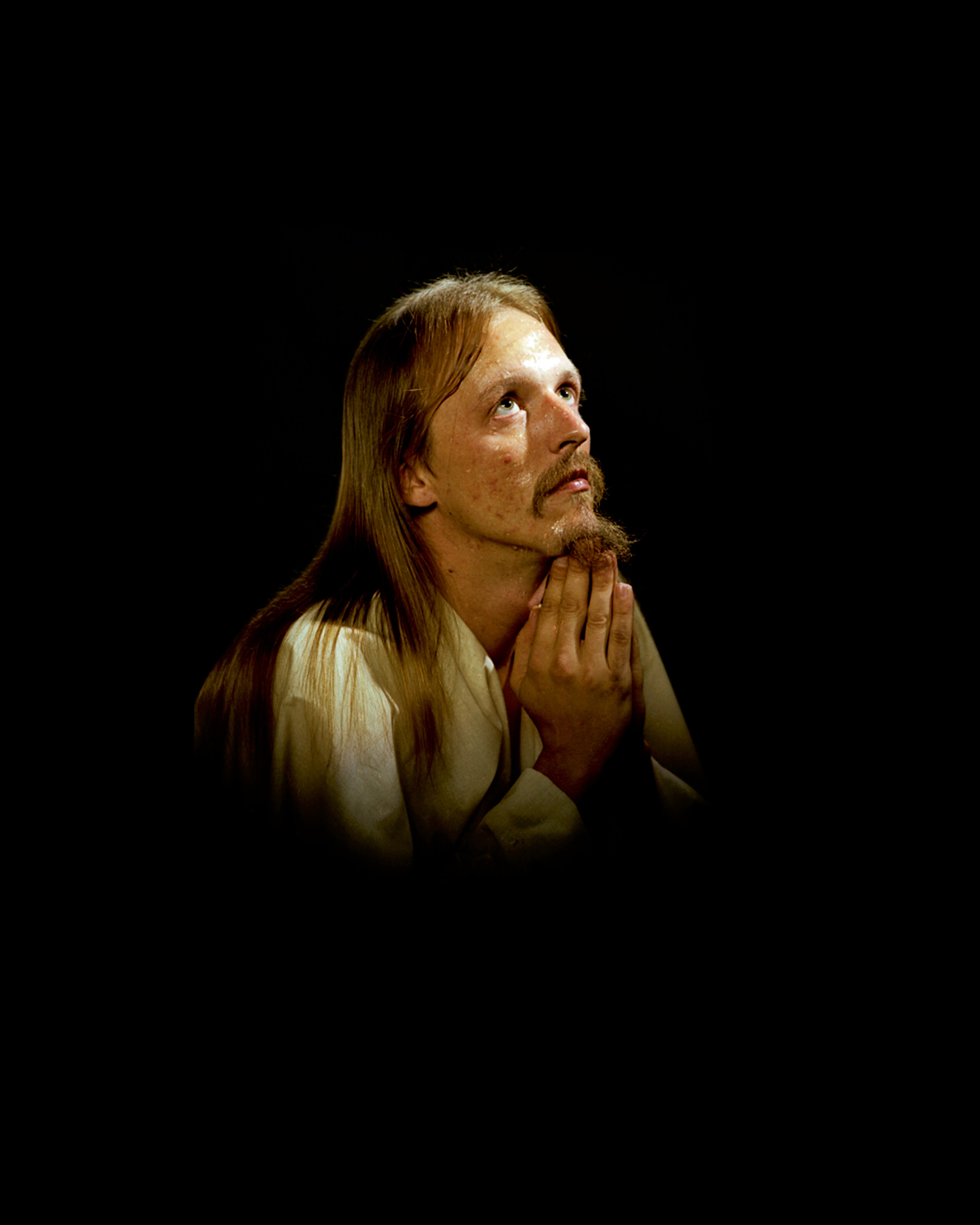 A photograph of a Christ-like man, with zits on his cheeks, praying. 