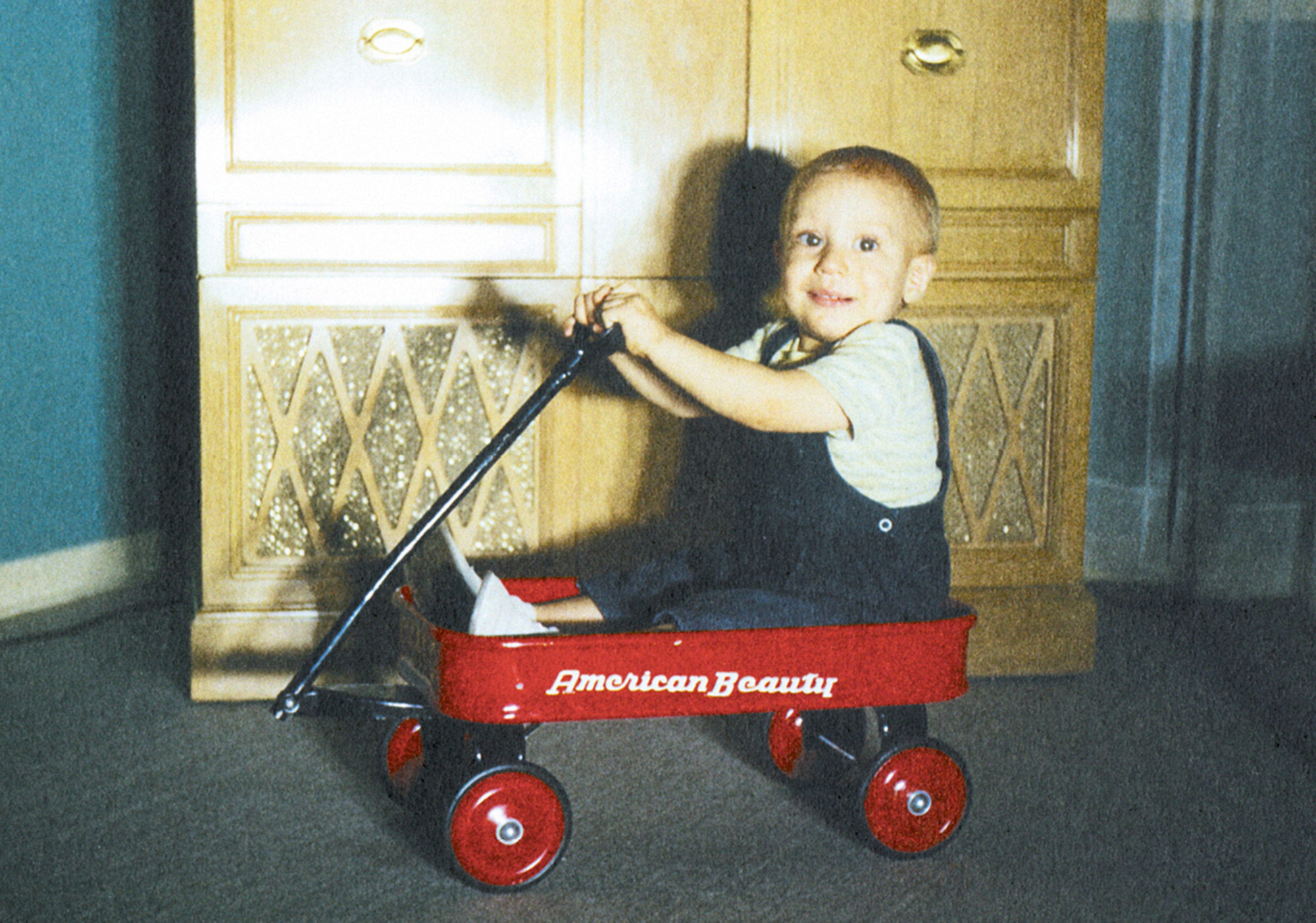 A photograph of a baby riding in a red toy wagon.
